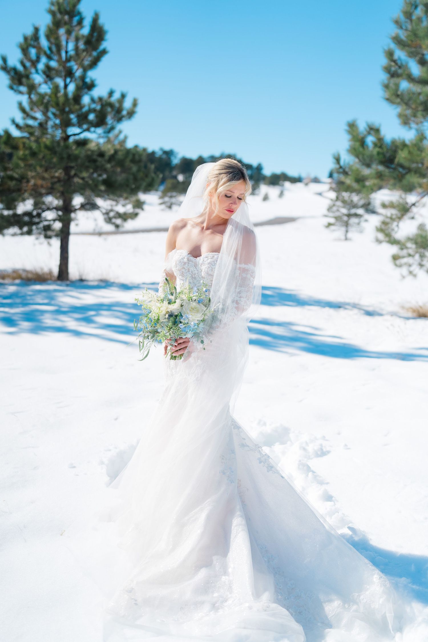 A person in a flowing white wedding dress twirls gracefully in a snowy winter landscape surrounded by evergreen trees in Vail, Colorado.