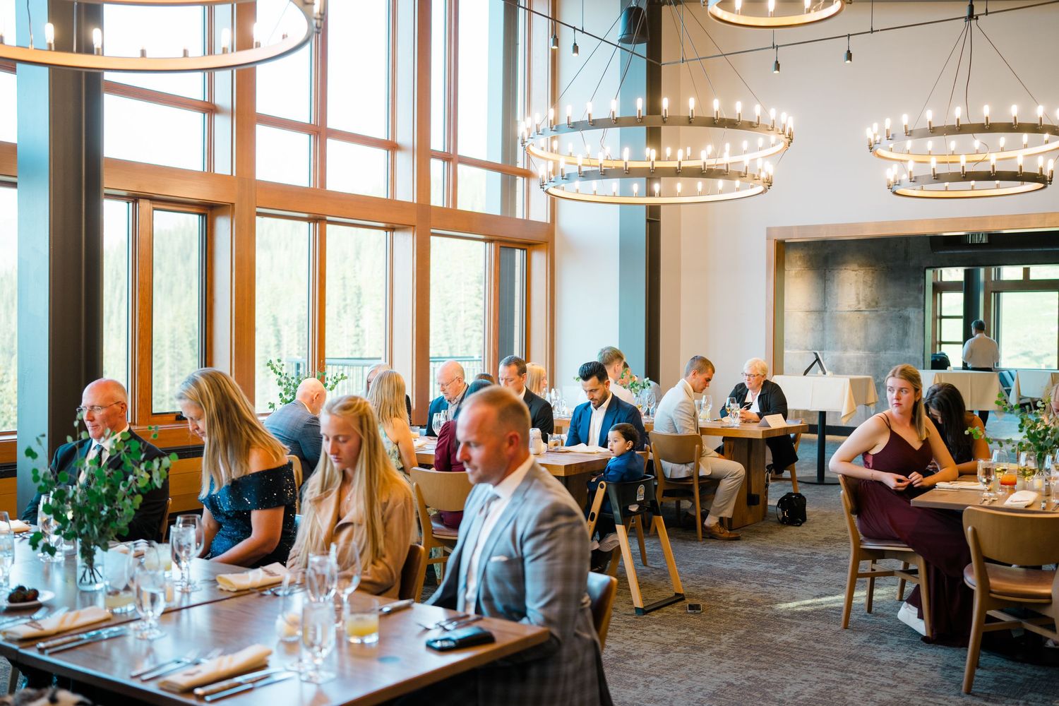 Modern restaurant interior at Aerie copper mountain with large windows, chandeliers, and diners seated at tables in a bright, airy space.
