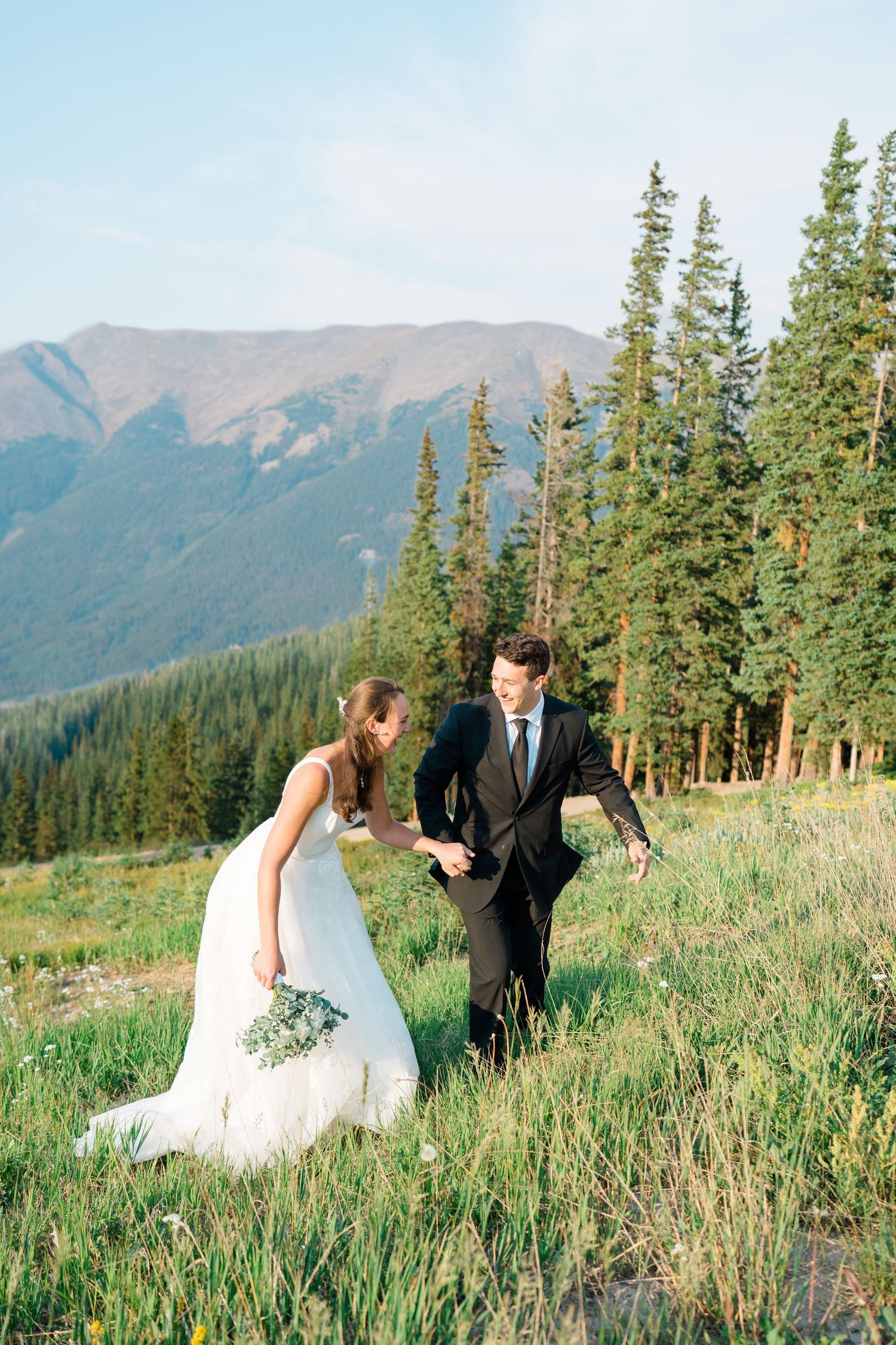 Couple dancing and twirling in a mountain meadow at copper mountain with evergreen trees and peaks in the background.