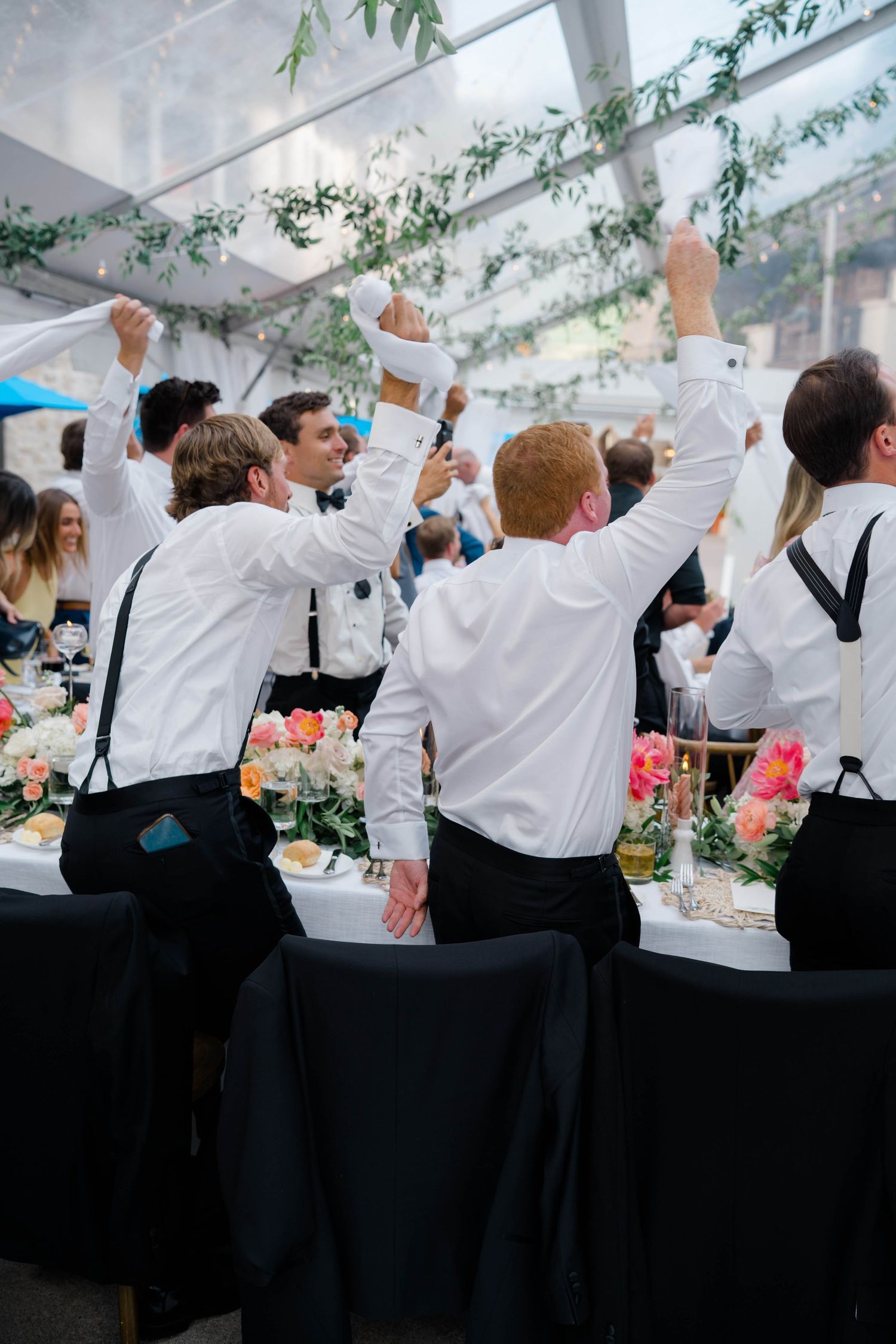 Groomsmen in white shirts and suspenders raise their hands in celebration at an elegant wedding reception at Arrabelle in Vail.