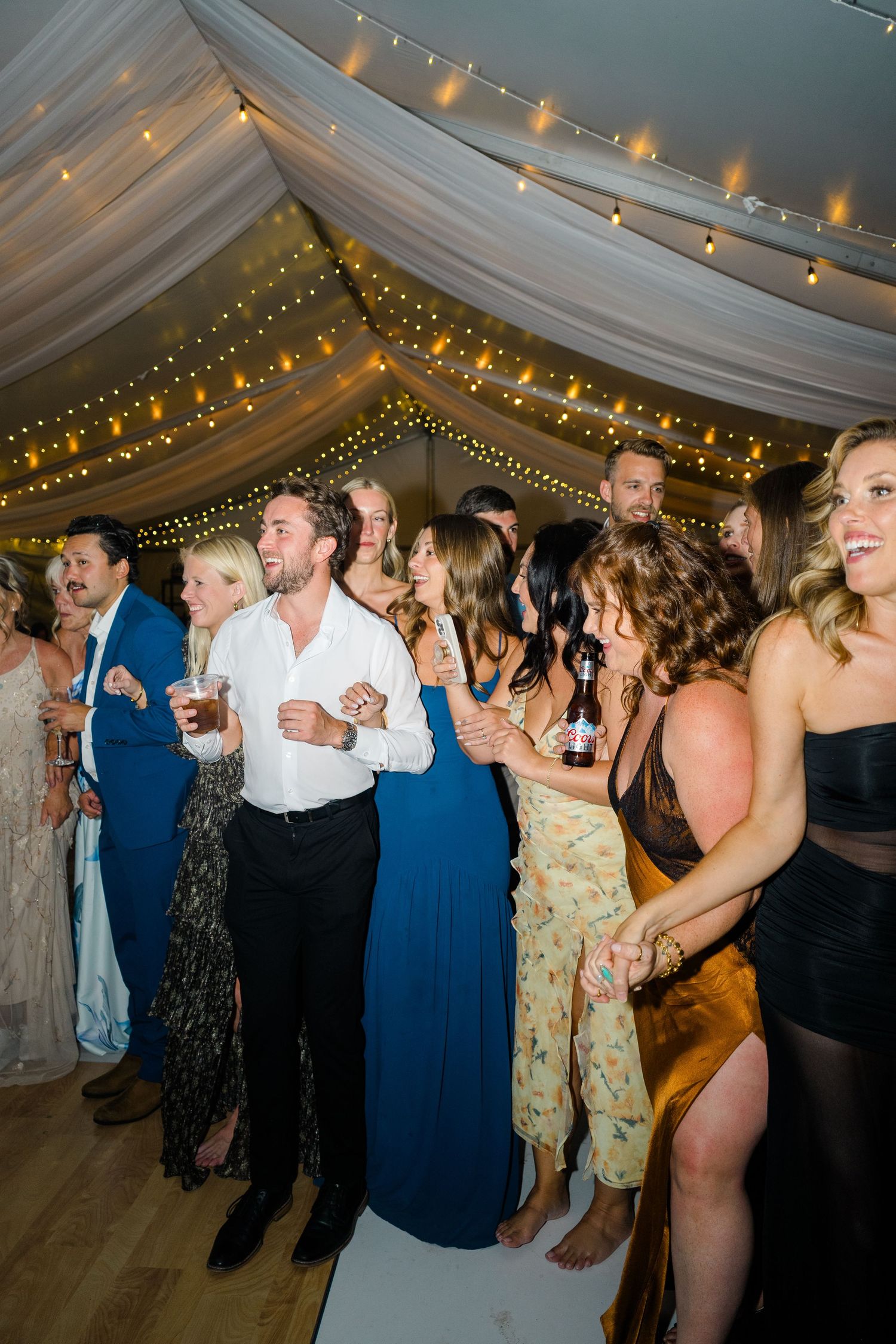 Guests laughing and dancing under fairy lights and draped fabric ceiling at an elegant wedding reception.