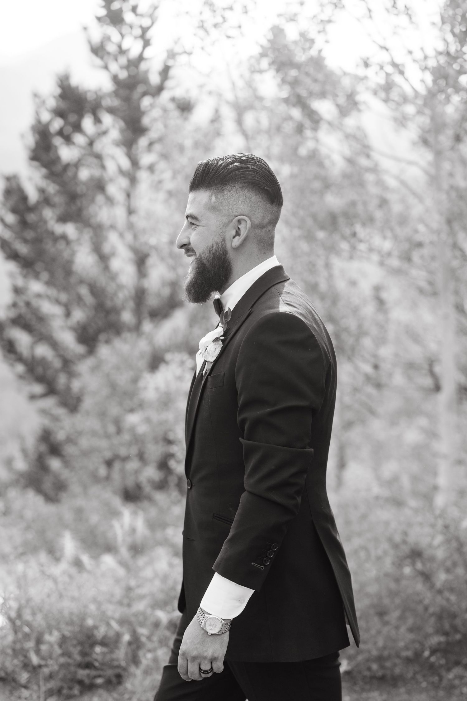 Black and white profile shot of a groom in a fitted suit with styled hair and beard standing outdoors  during breckenridge micro wedding.