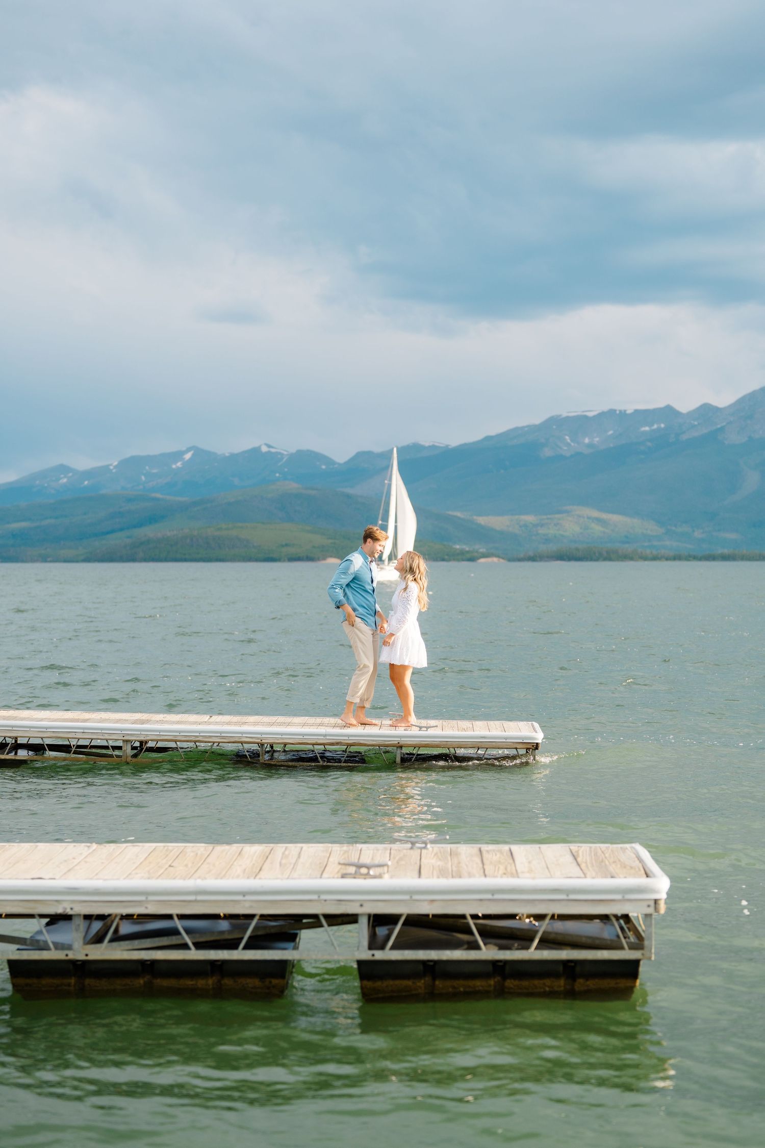 A wooden dock stretches into a mountain lake on a cloudy day.