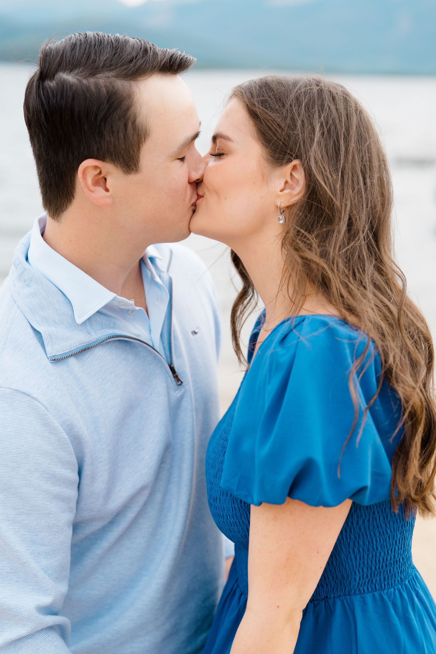 A couple in blue and light blue attire share a tender kiss while on a boat.
