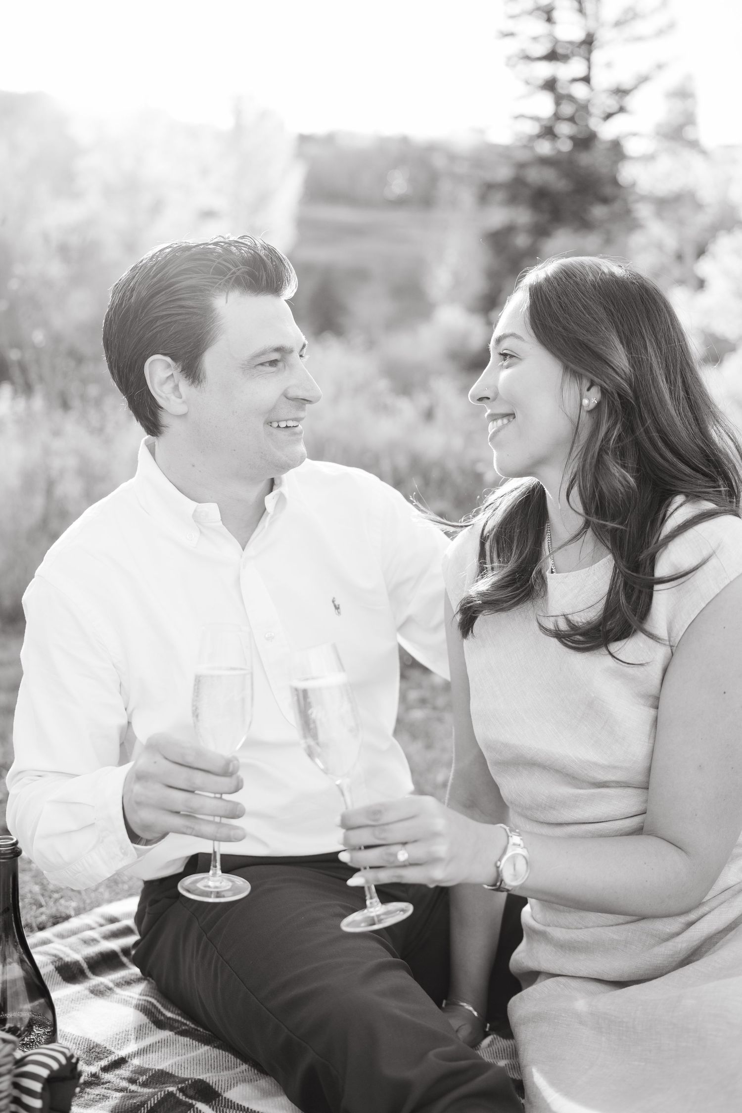 A couple shares champagne and laughter during a romantic black and white outdoor picnic.