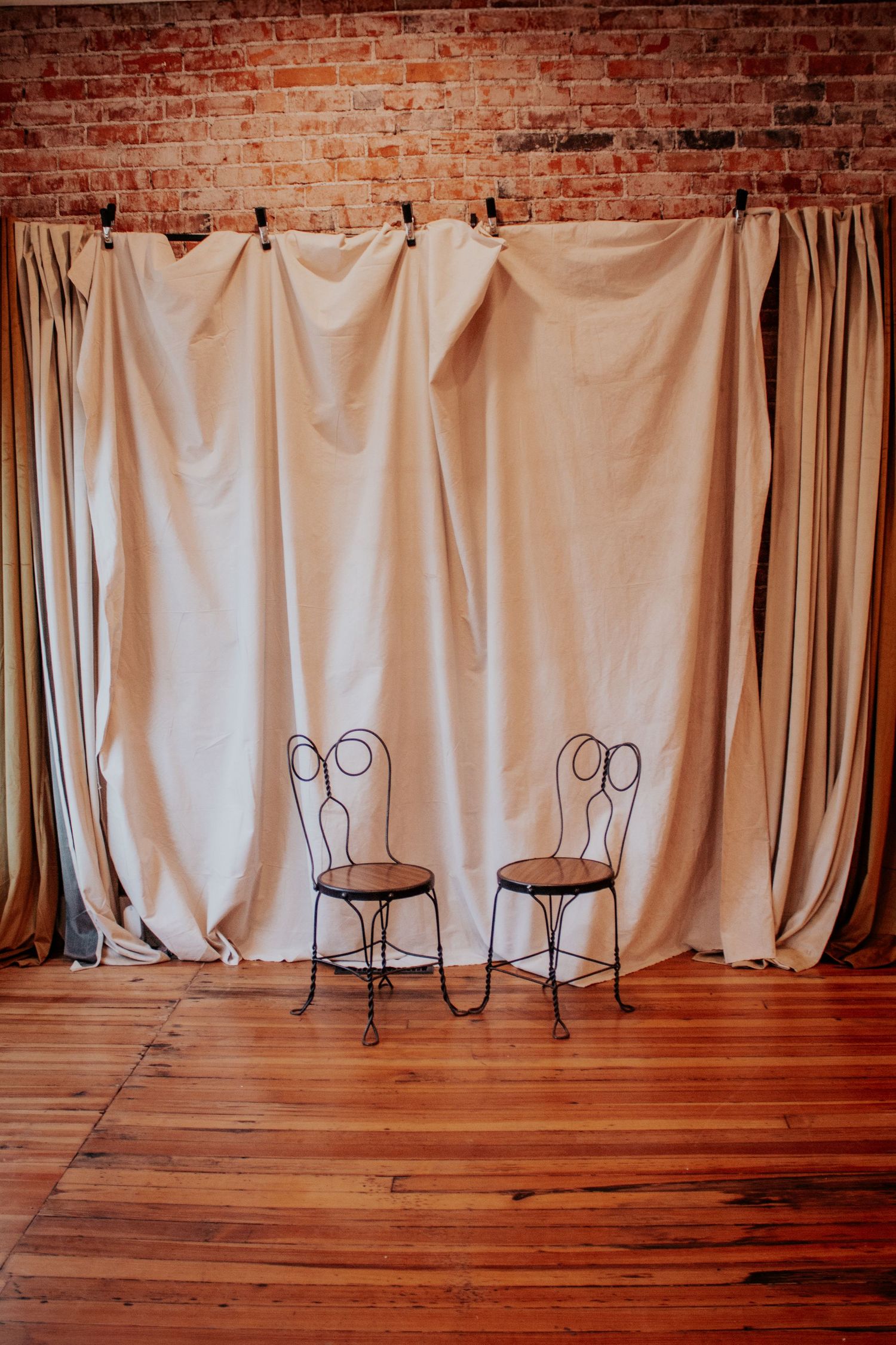 White curtain backdrop against exposed brick wall with wooden floor and iron plant stands in vintage event space.