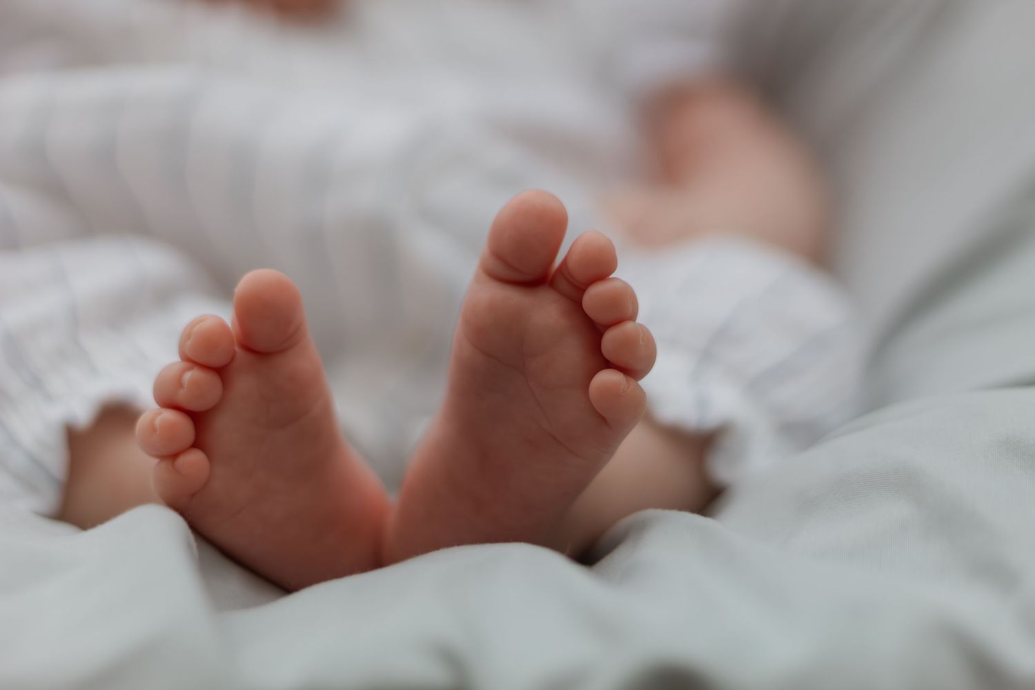 Close-up of tiny newborn baby feet resting on soft white blanket, perfect for birth announcements.
