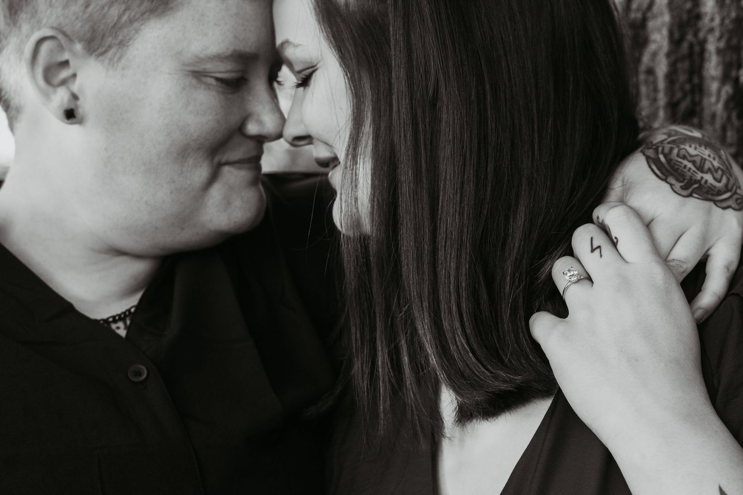 Black and white photo of a couple sharing an intimate moment, with visible tattoos and rings on her hand.
