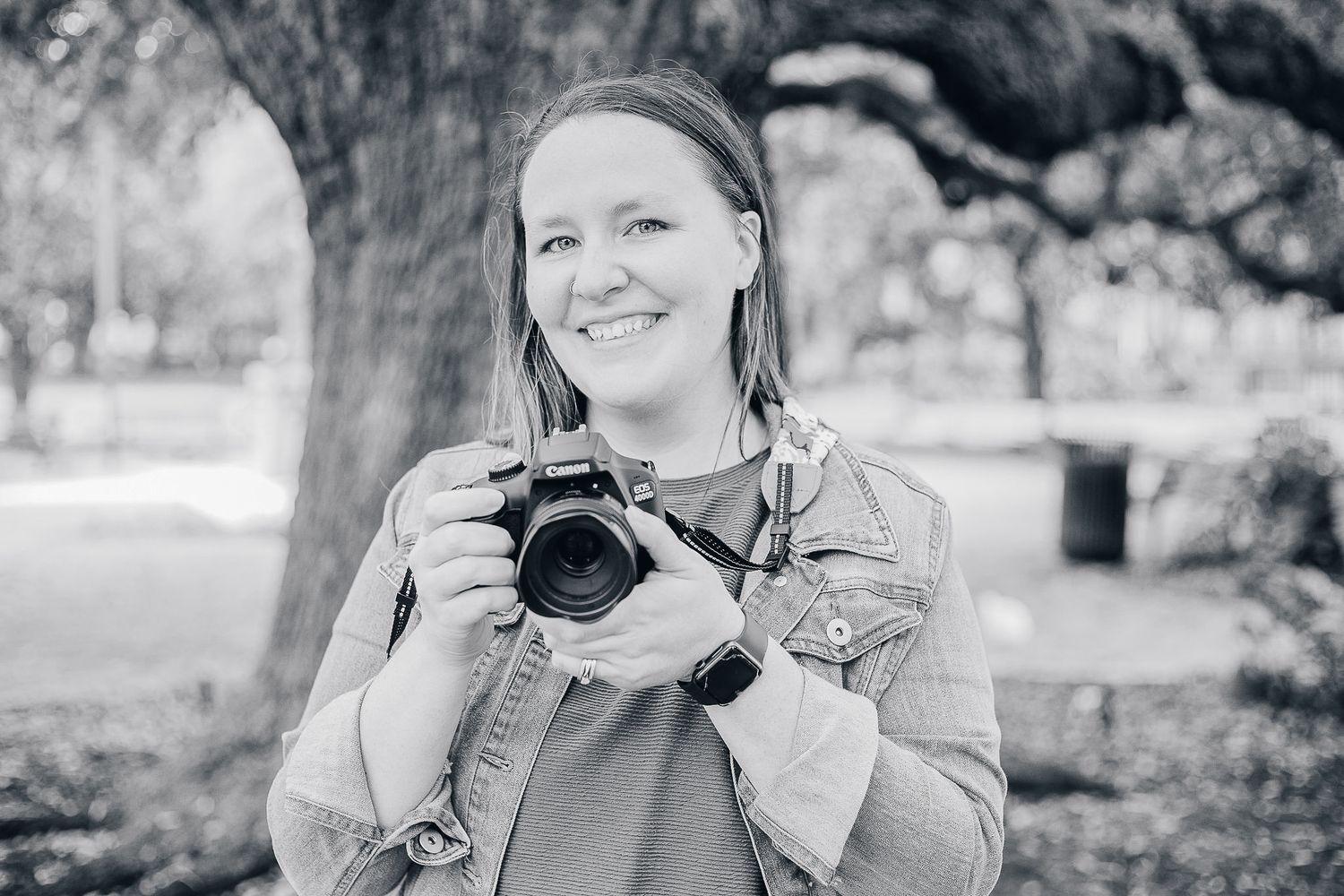 Photographer with camera smiling outdoors in black and white portrait.