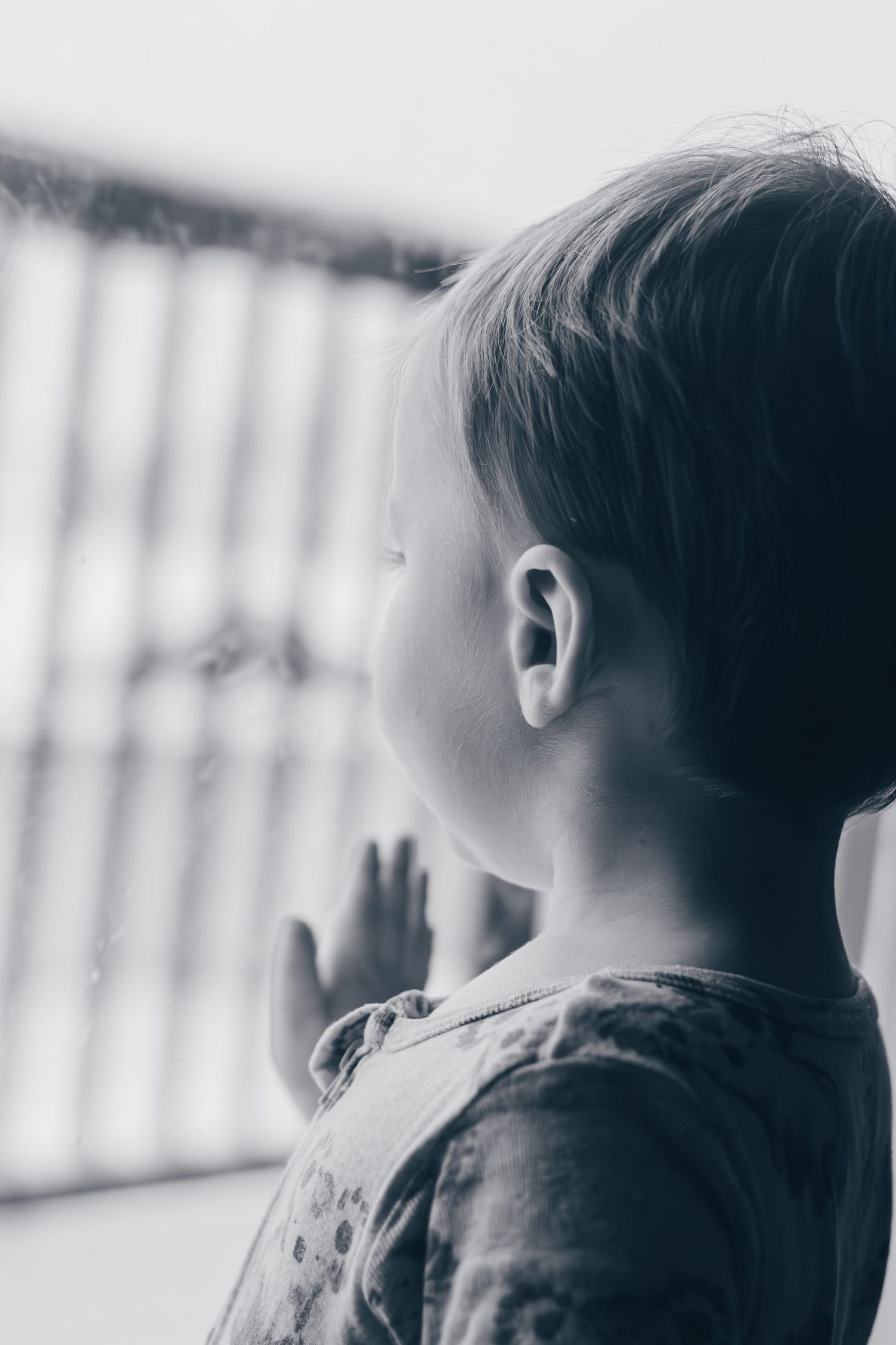 A black and white profile view of a young child looking out a window with soft natural lighting.