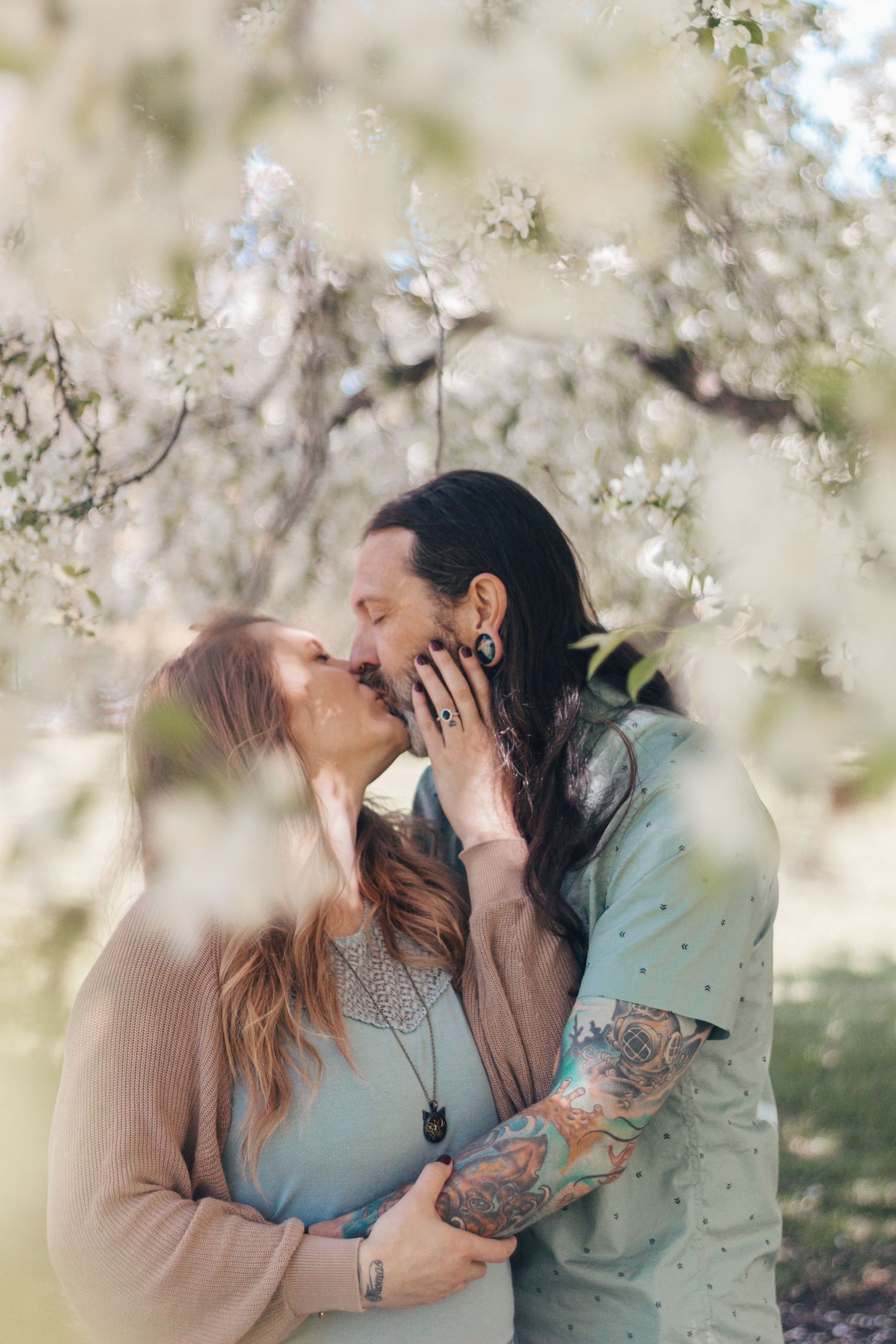 A romantic couple shares a tender kiss among blooming spring cherry blossoms in a dreamy outdoor setting.