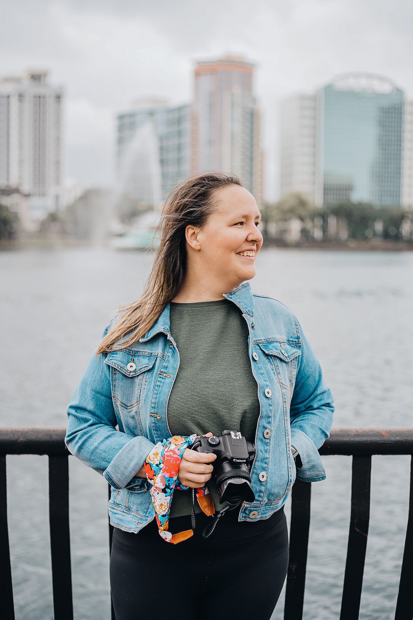 Photographer with camera standing by waterfront with city skyline in background.