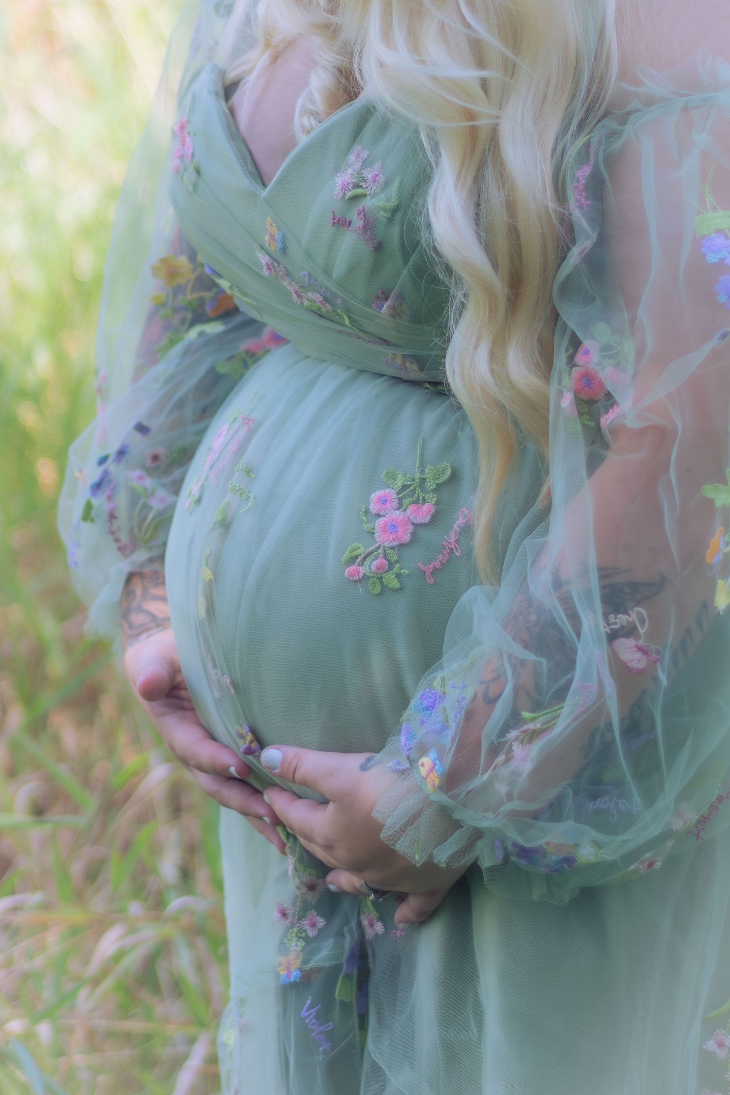 A mint green maternity gown with delicate floral embroidery is showcased in a dreamy outdoor setting.