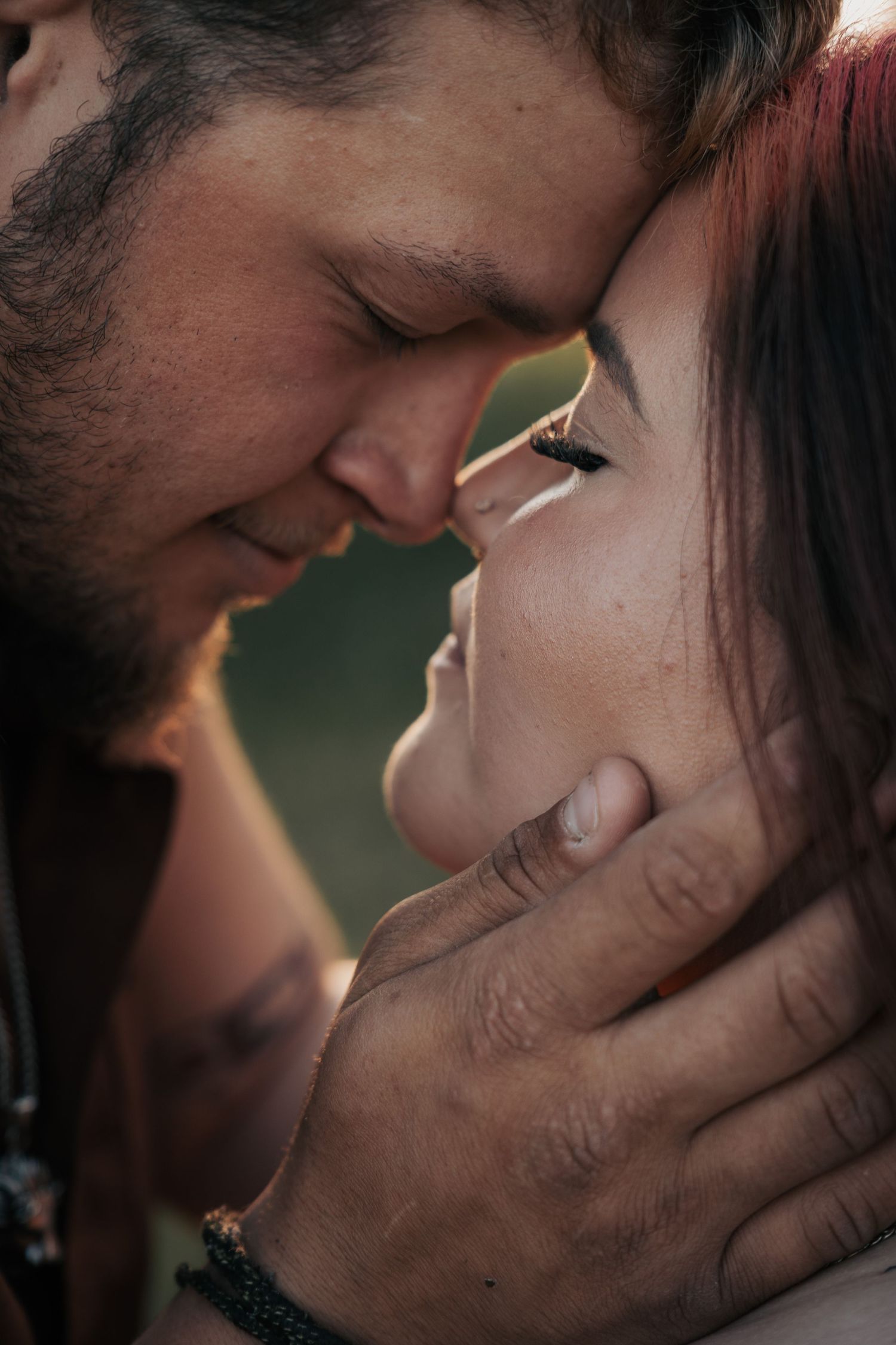 A couple sharing an intimate moment, foreheads touching, as a man gently cups a freckled redhead woman's face.
