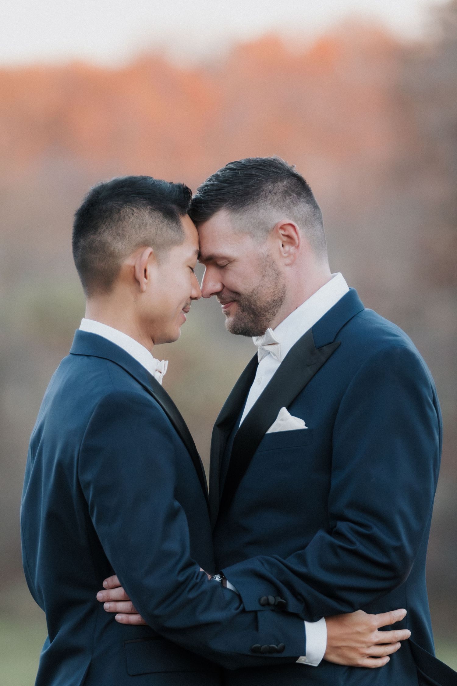 Two people in dark suits share an intimate moment together during an outdoor photo session at sunset.