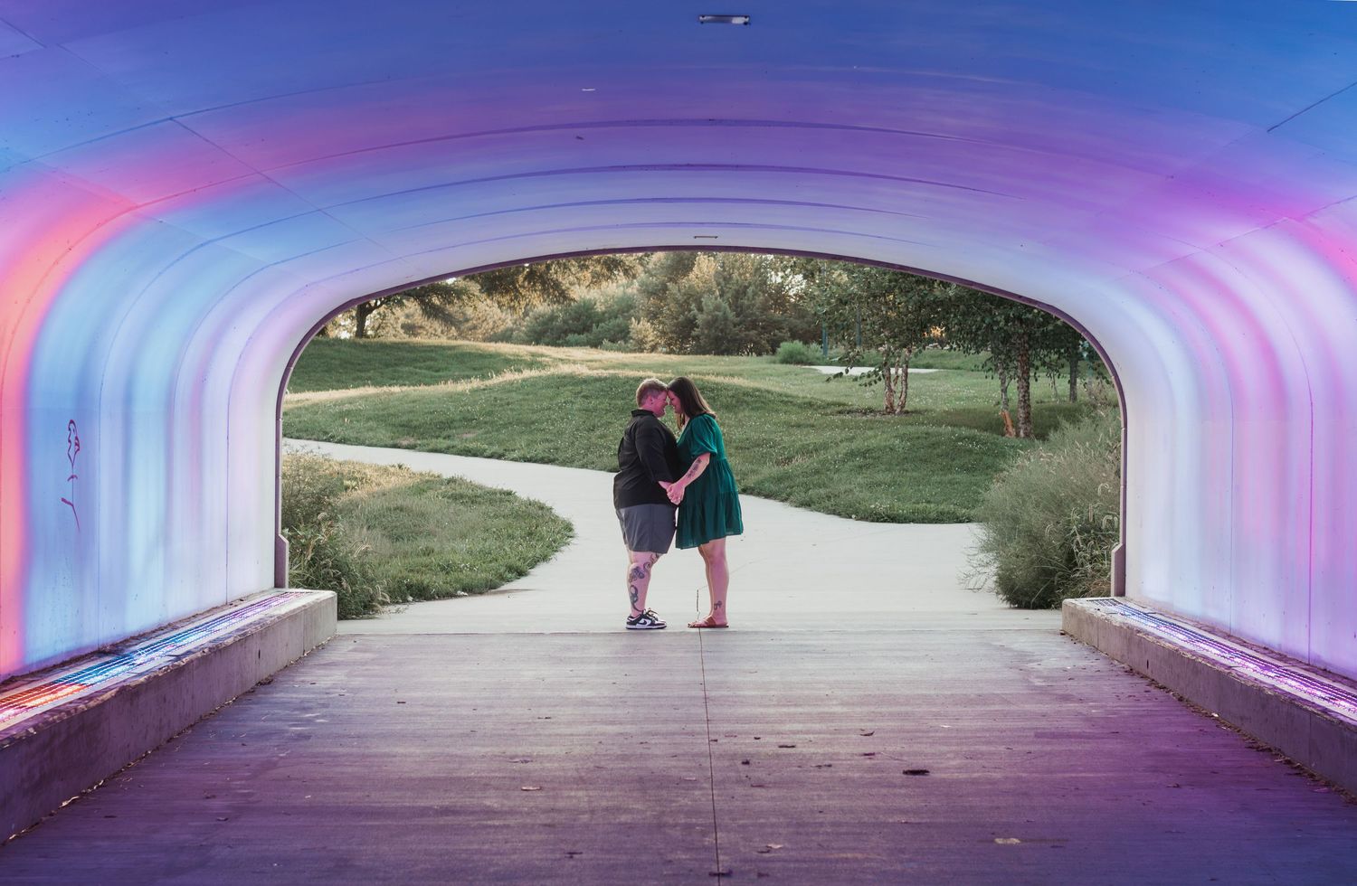 Couple embracing under a colorful illuminated tunnel arch in a scenic park with winding pathways.