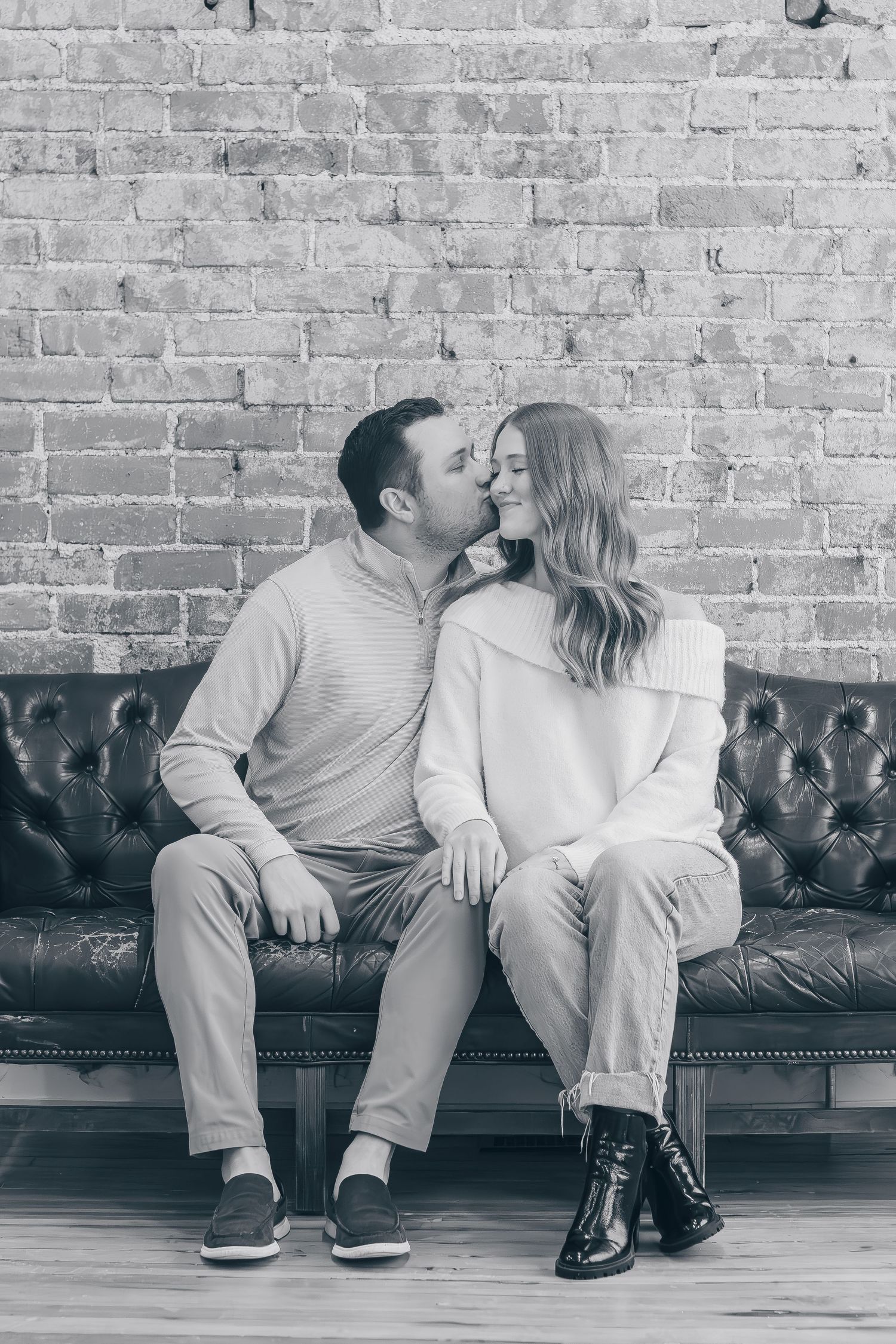 Black and white photo sequence showing a couple sitting on a leather couch against a brick wall sharing a romantic moment.