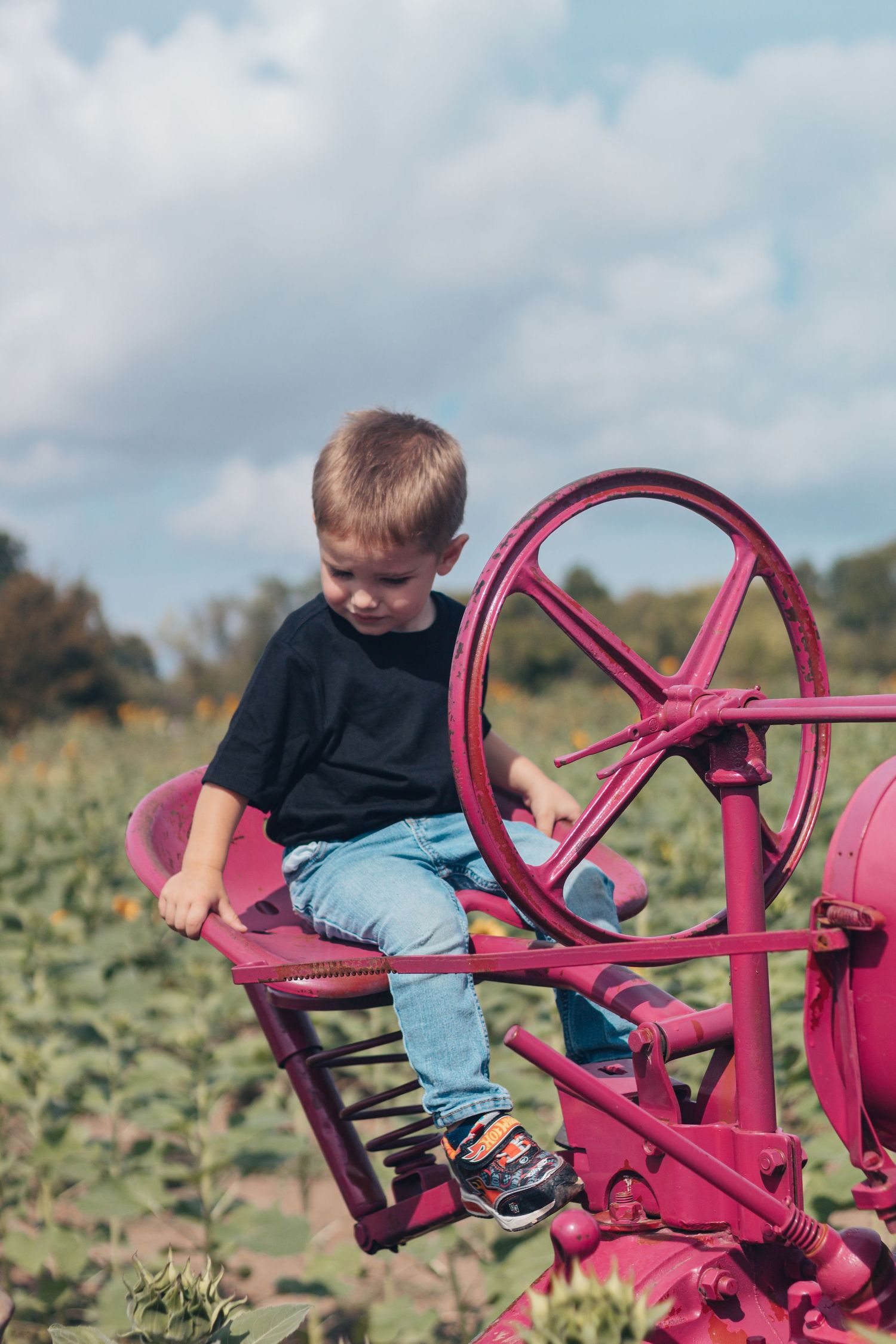 A child sits on bright pink vintage farm equipment in a field on a cloudy day.