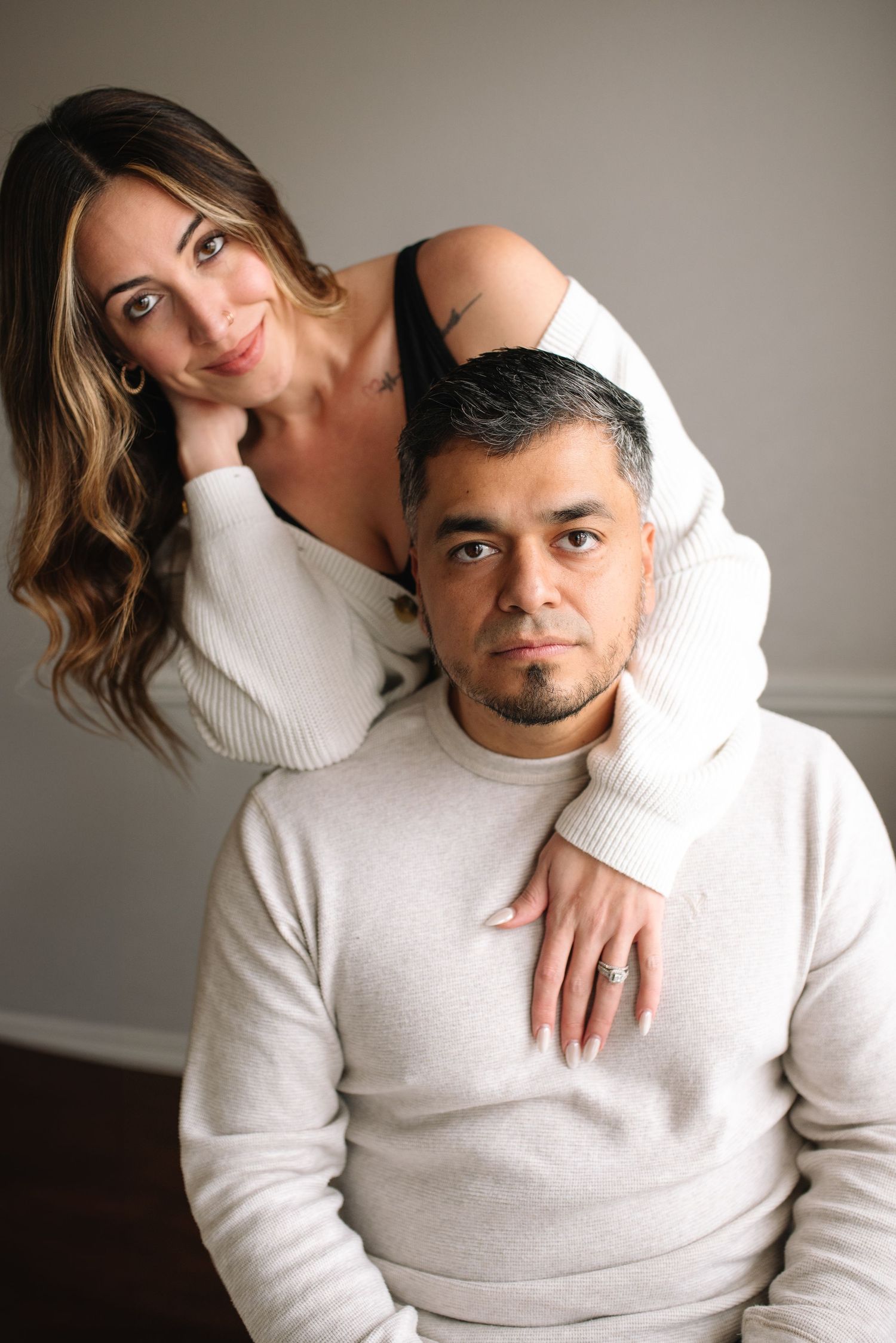 Couple in white sweaters pose intimately together against neutral background in romantic photoshoot series.