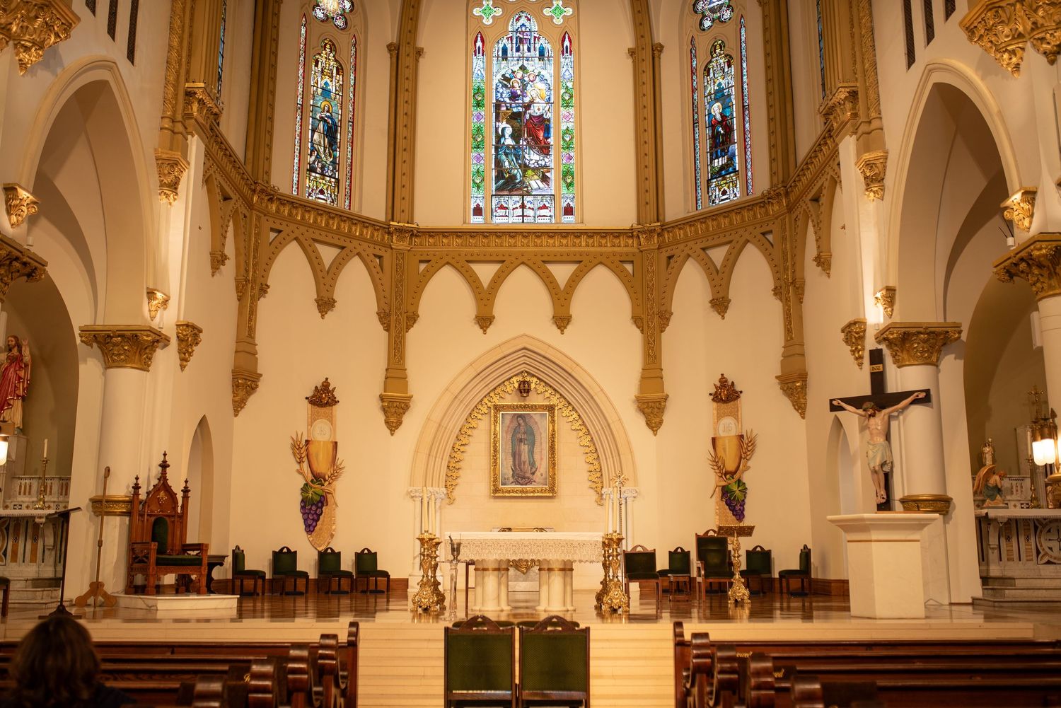 Interior view of an ornate Catholic church sanctuary with stained glass windows, arches, and golden architectural details.