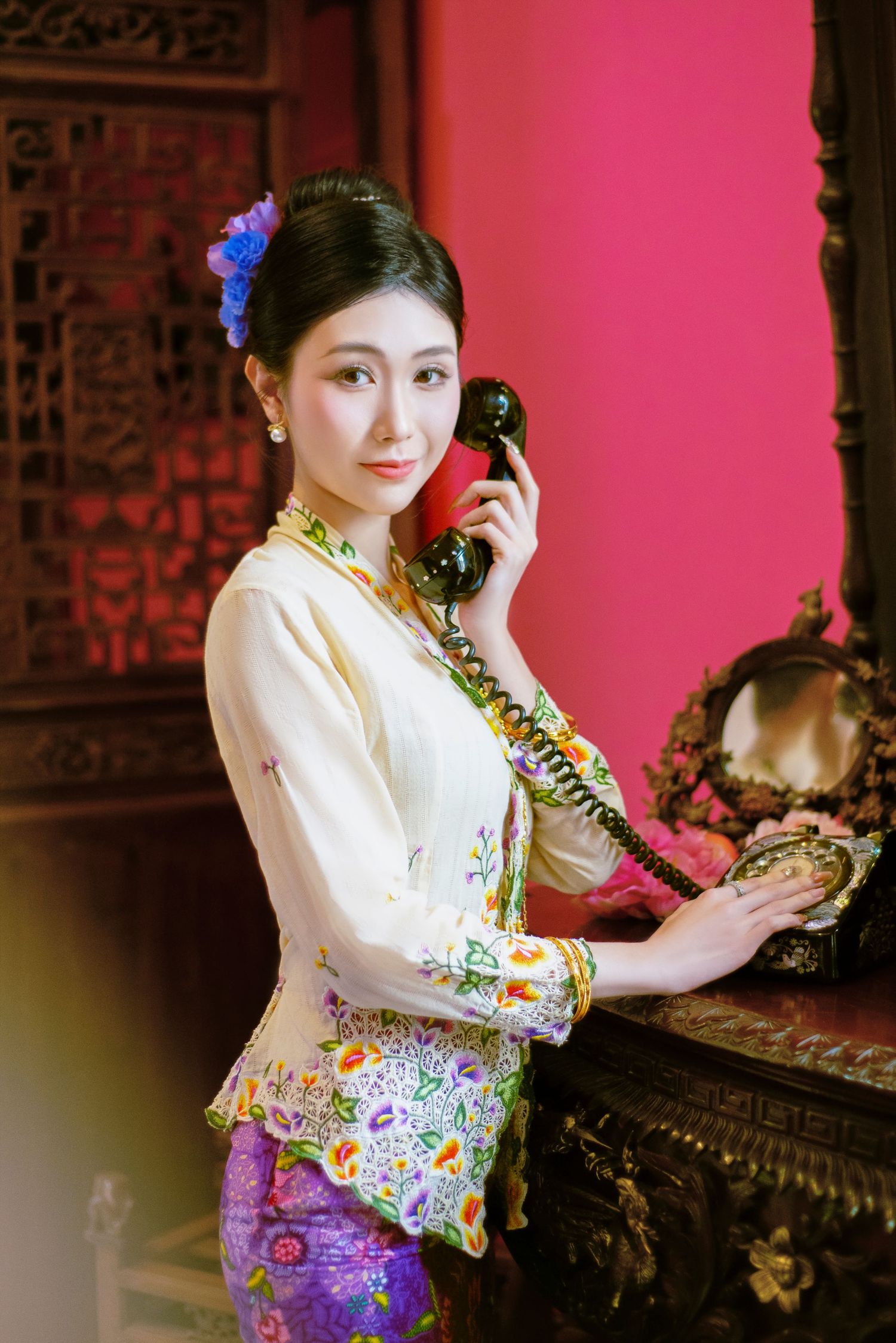 Vintage inspired portrait showing traditional Asian fashion with embroidered floral details and antique telephone.
