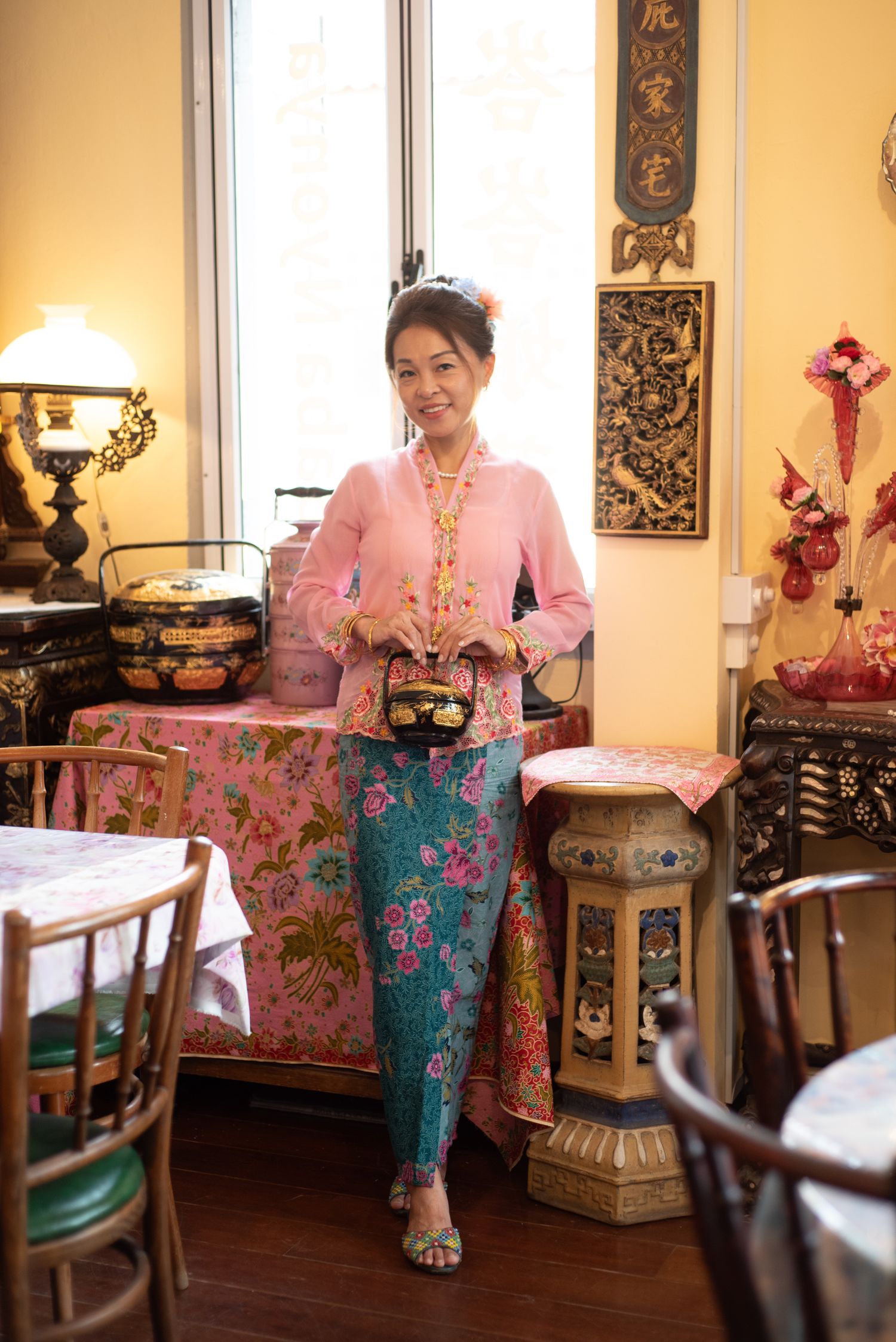 Traditional peranakan interior with pink kebaya top and batik sarong displayed among antique furniture and decorative elements.