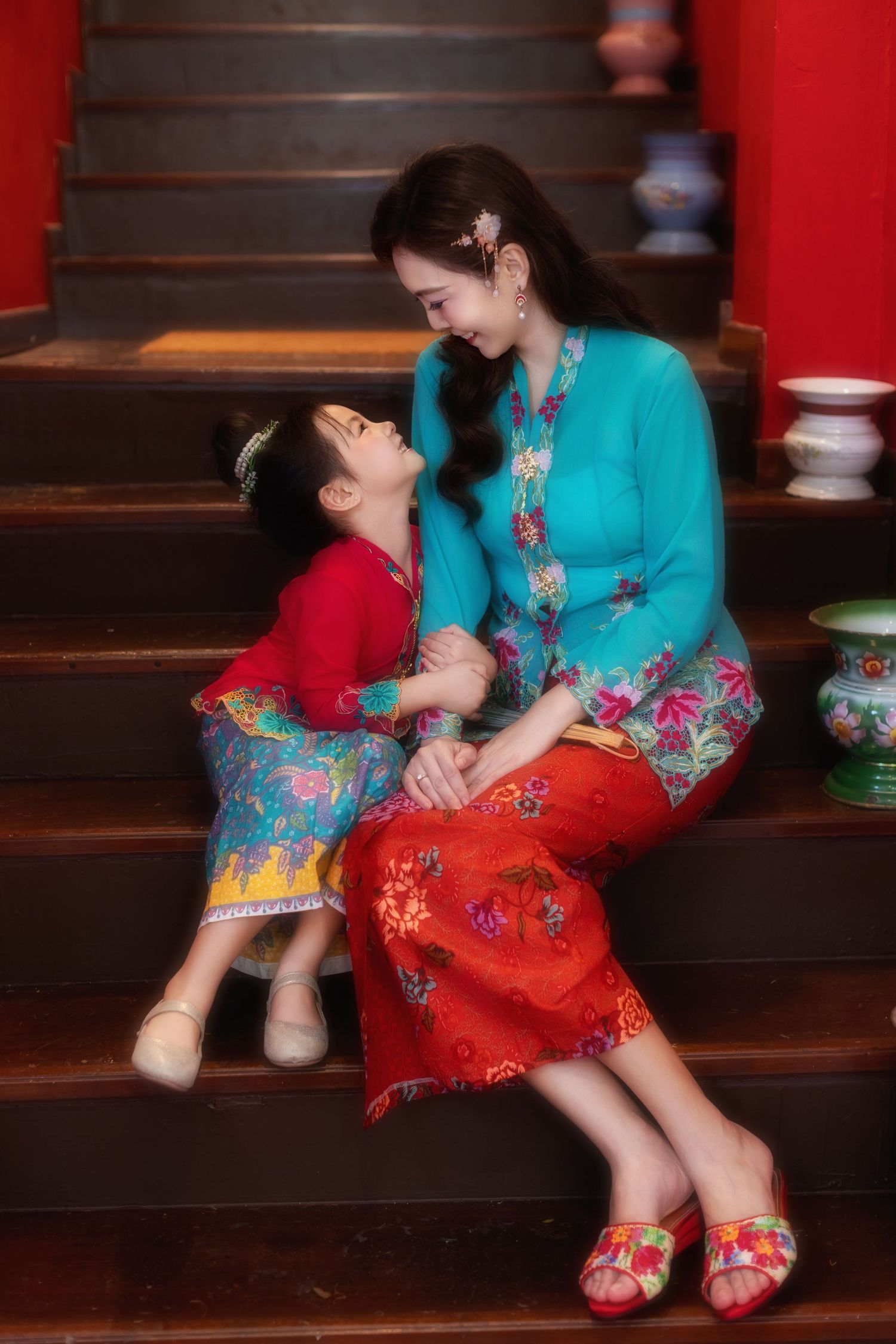 Portrait of Mother and daughter in traditional Nyonya Kebaya sitting on red-walled stairs in private museum Peranakan Mansion at Joo Chiat.