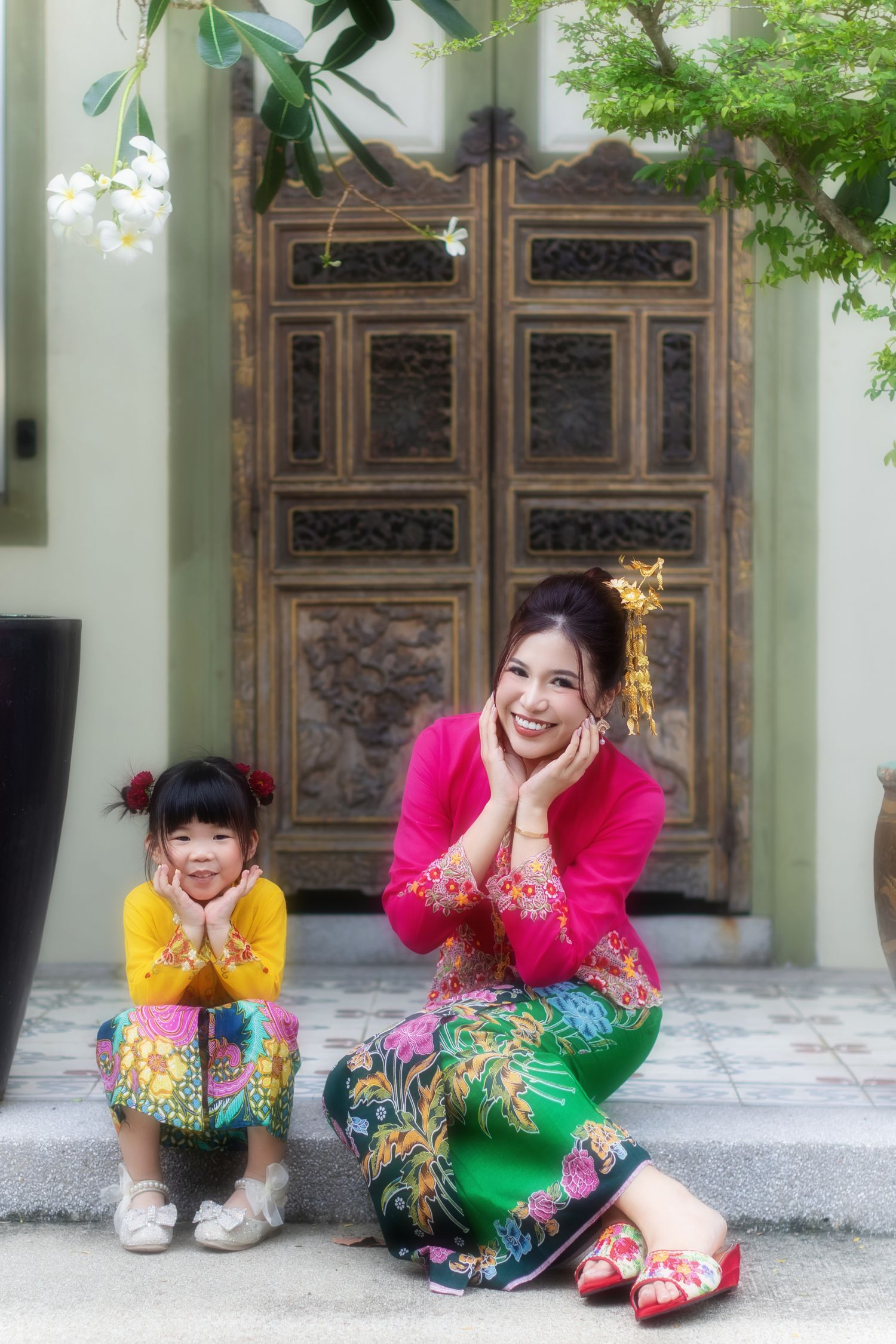 Portrait of a Nyonya mother and child in pink and yellow kebaya, in front of a wooden door Pintu pagar, at a Peranakan house in Joo Chiat