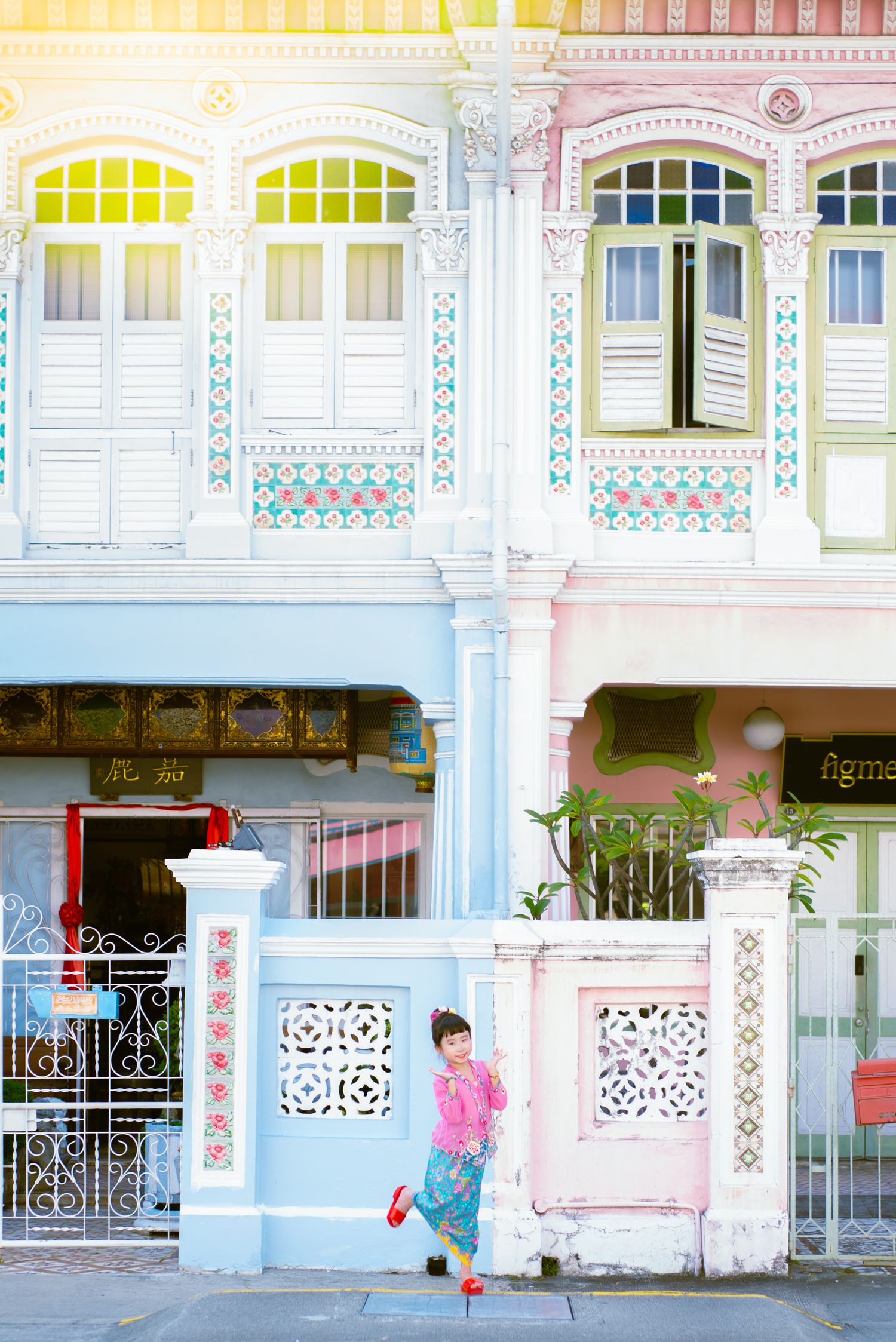 Pink and yellow pastel shophouses showcase traditional Peranakan architecture with ornate details along a Singapore street.