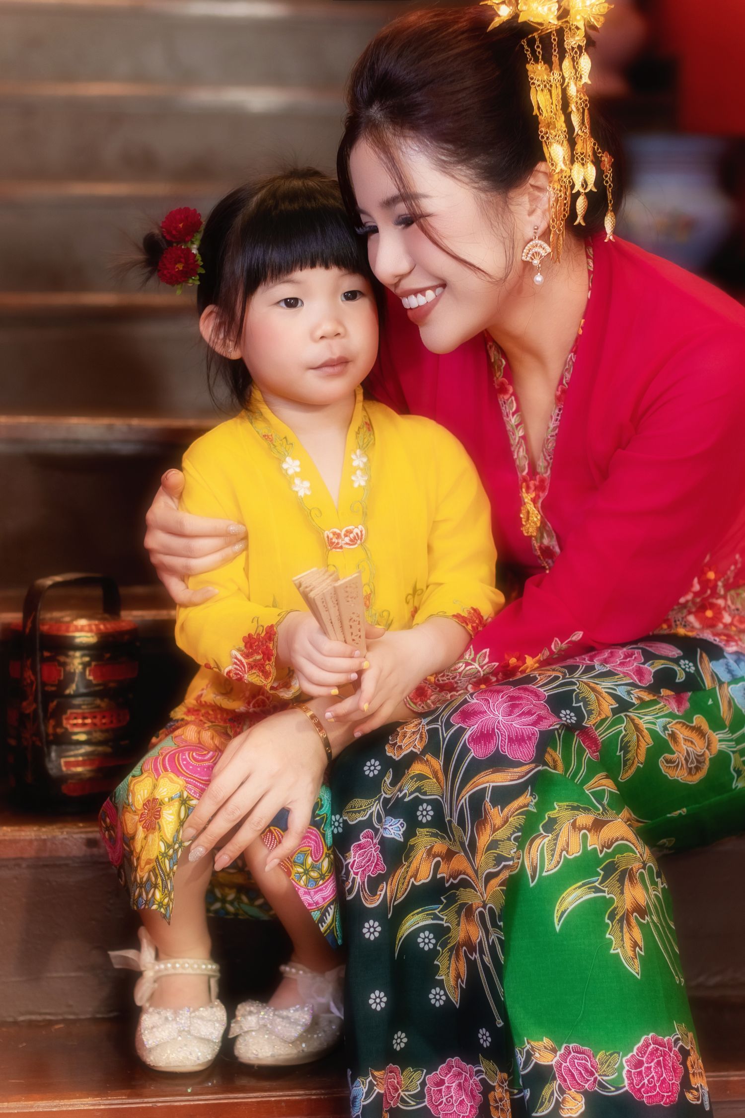 Portrait of Mother and child in traditional Nyonya Kebaya sitting on red-walled stairs in private museum Peranakan Mansion at Joo Chiat.