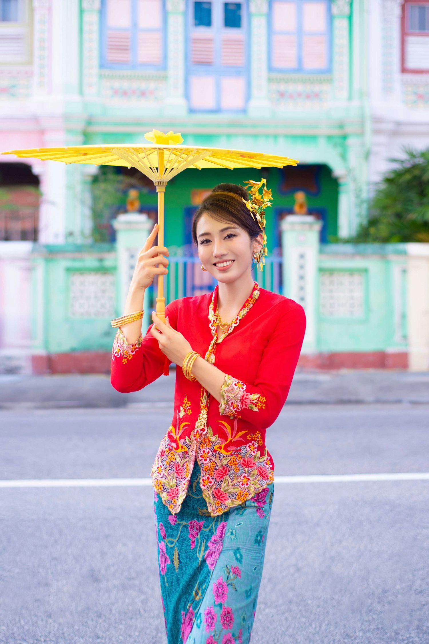 A person in traditional Peranakan Nyonya dress with red kebaya and batik sarong holds a yellow parasol in Singapore.