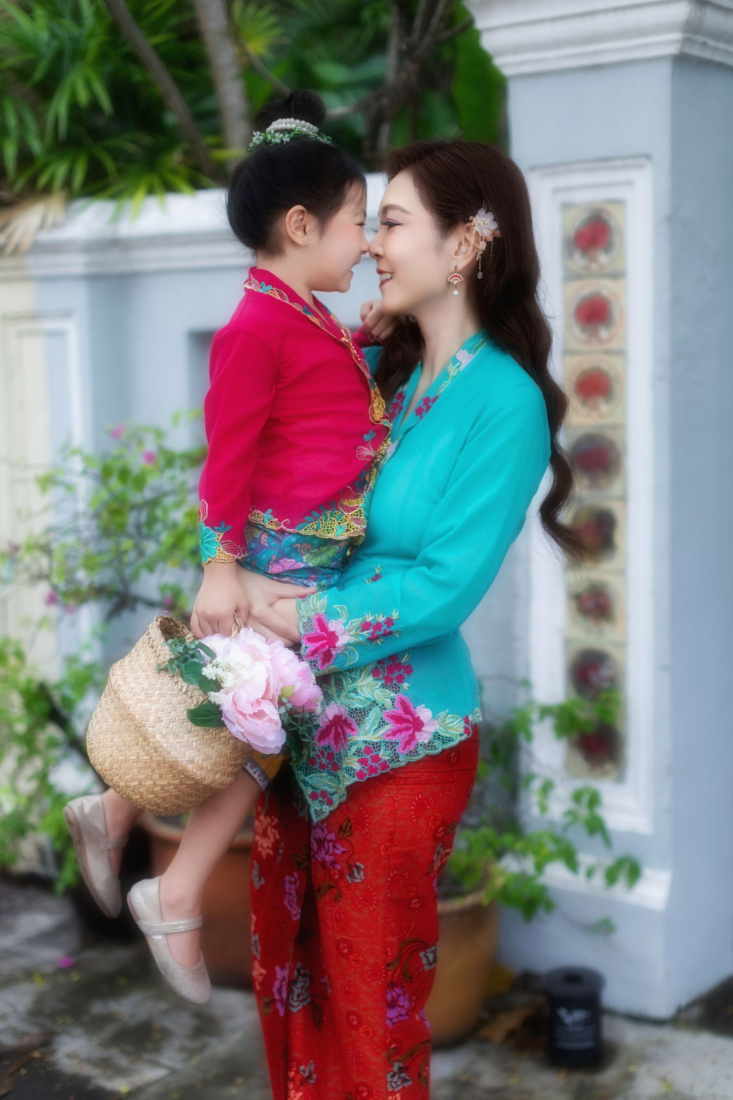Photoshoot of mother and daughter in traditional Nyonya Kebaya holding a flower basket, against a Peranakan-tiled wall.