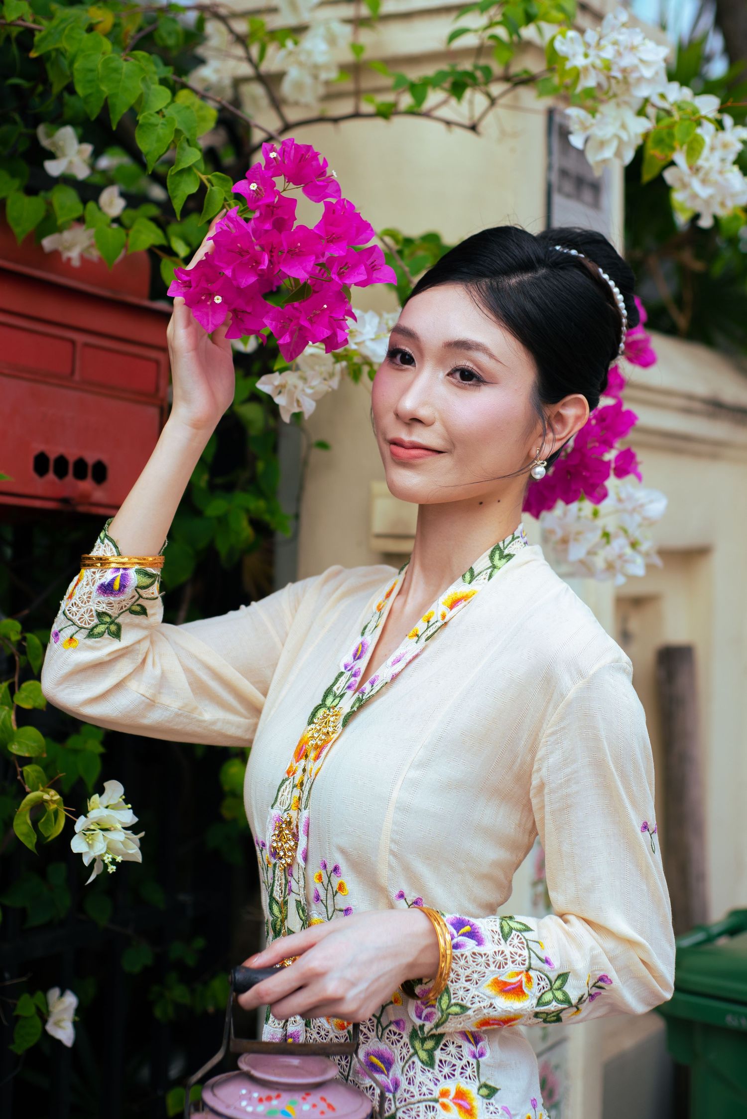 Traditional Thai formal dress showcased among blooming pink bougainvillea and white flowers in a garden setting.