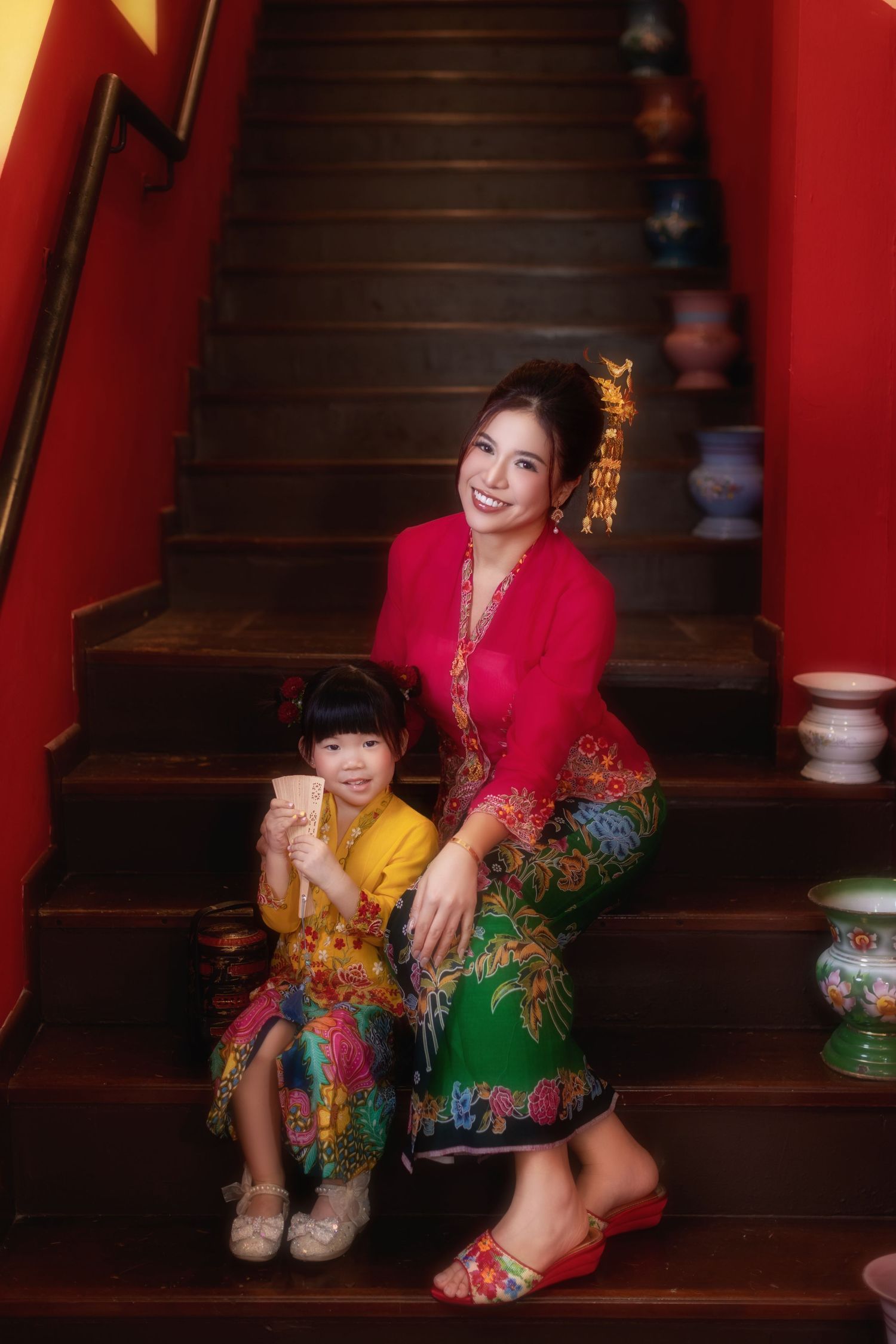 Photo of Mother and child in traditional Nyonya Kebaya sitting on red-walled stairs in private museum Peranakan Mansion at Joo Chiat.