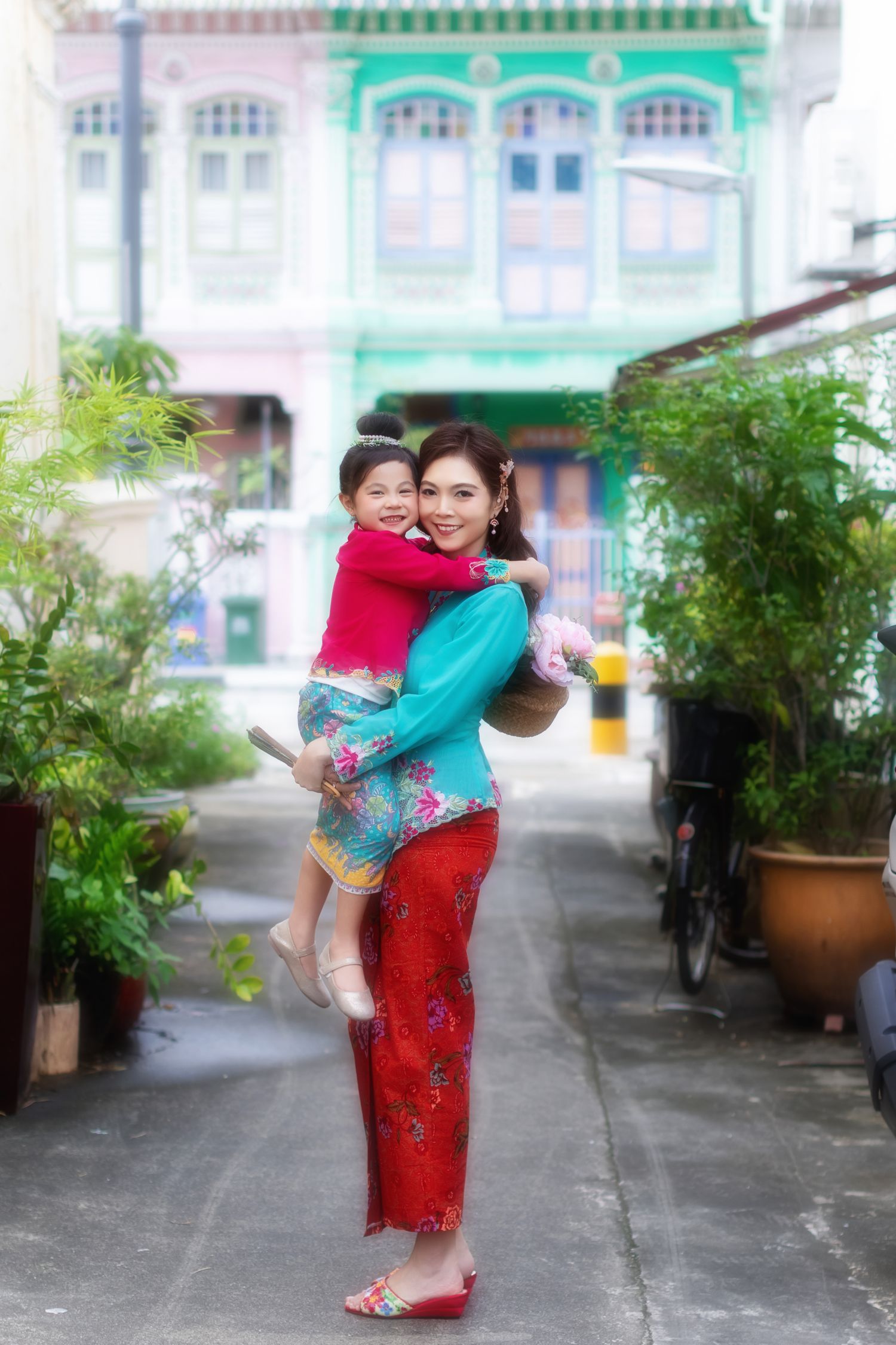 Photo of a mother and daughter in traditional Nyonya Kebaya sharing a joyful moment in front of heritage architecture, Peranakan houses.