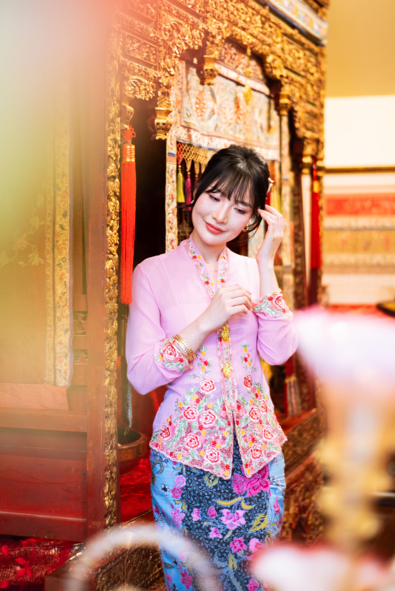 A person wearing a pink sweater and floral print garment poses with a joyful expression in warm lighting.