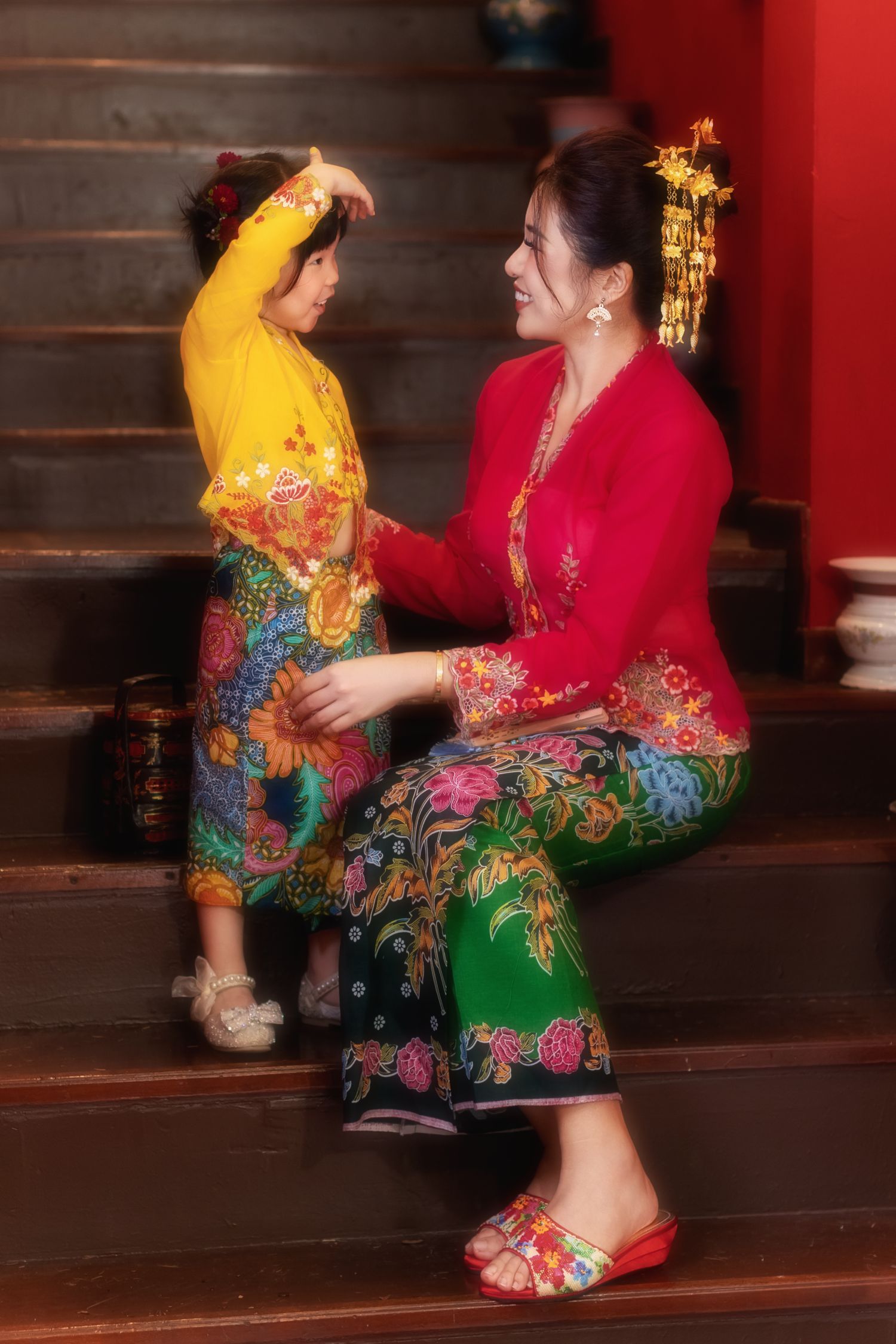 Image of Mummy and daughter in traditional Nyonya Kebaya sitting on red-walled stairs in private museum Peranakan Mansion at Joo Chiat.