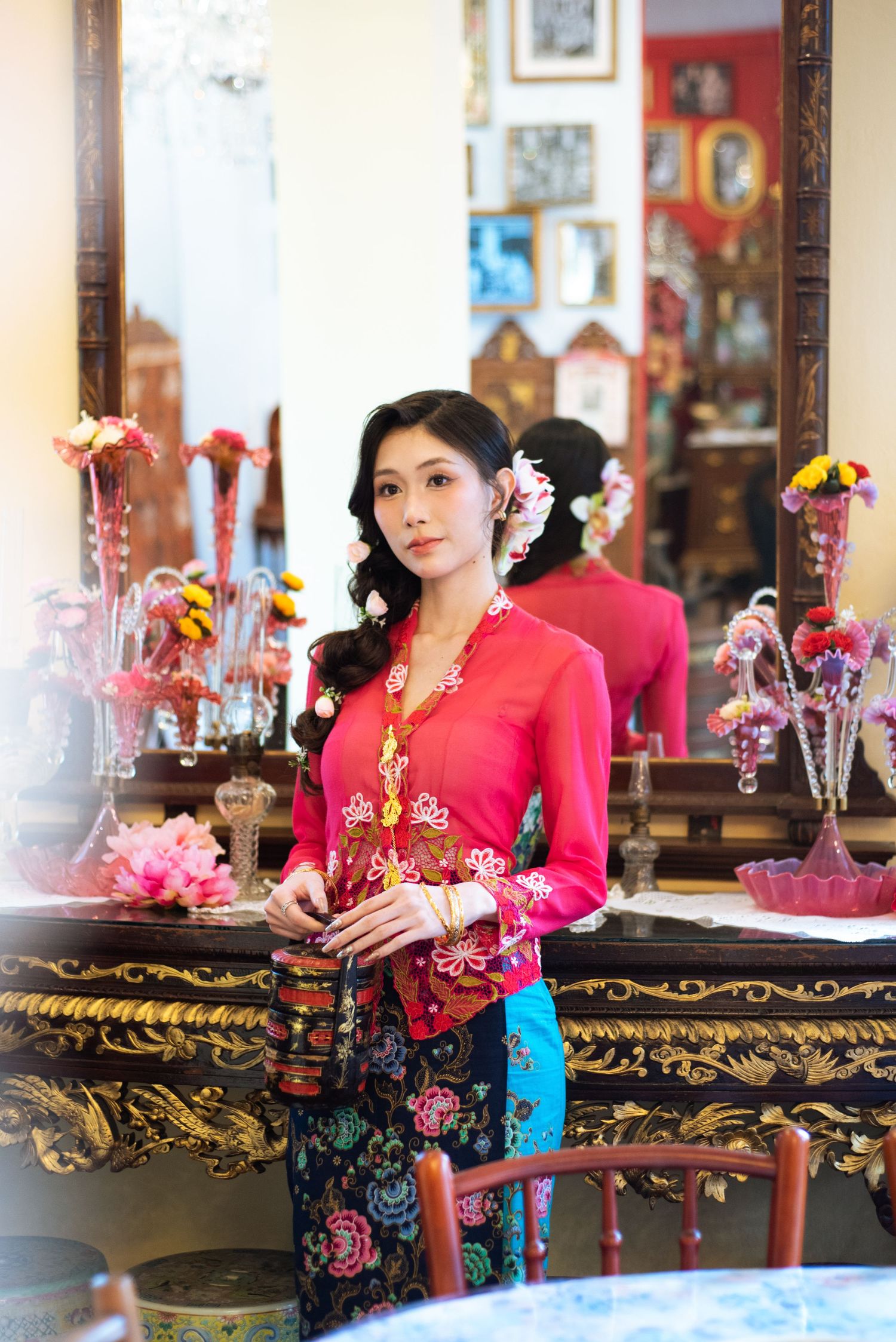 Traditional Indonesian kebaya outfit in bright red and floral print photographed in an ornate interior with decorative vases.