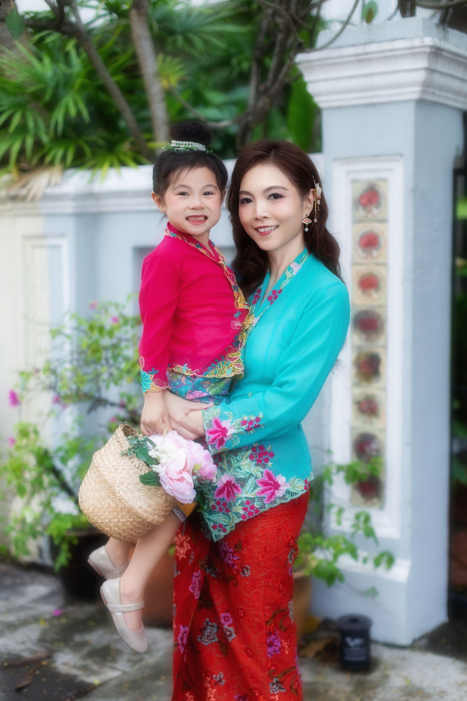 Photoshoot of mother and daughter in traditional Nyonya Kebaya holding a flower basket, against a Peranakan-tiled wall.