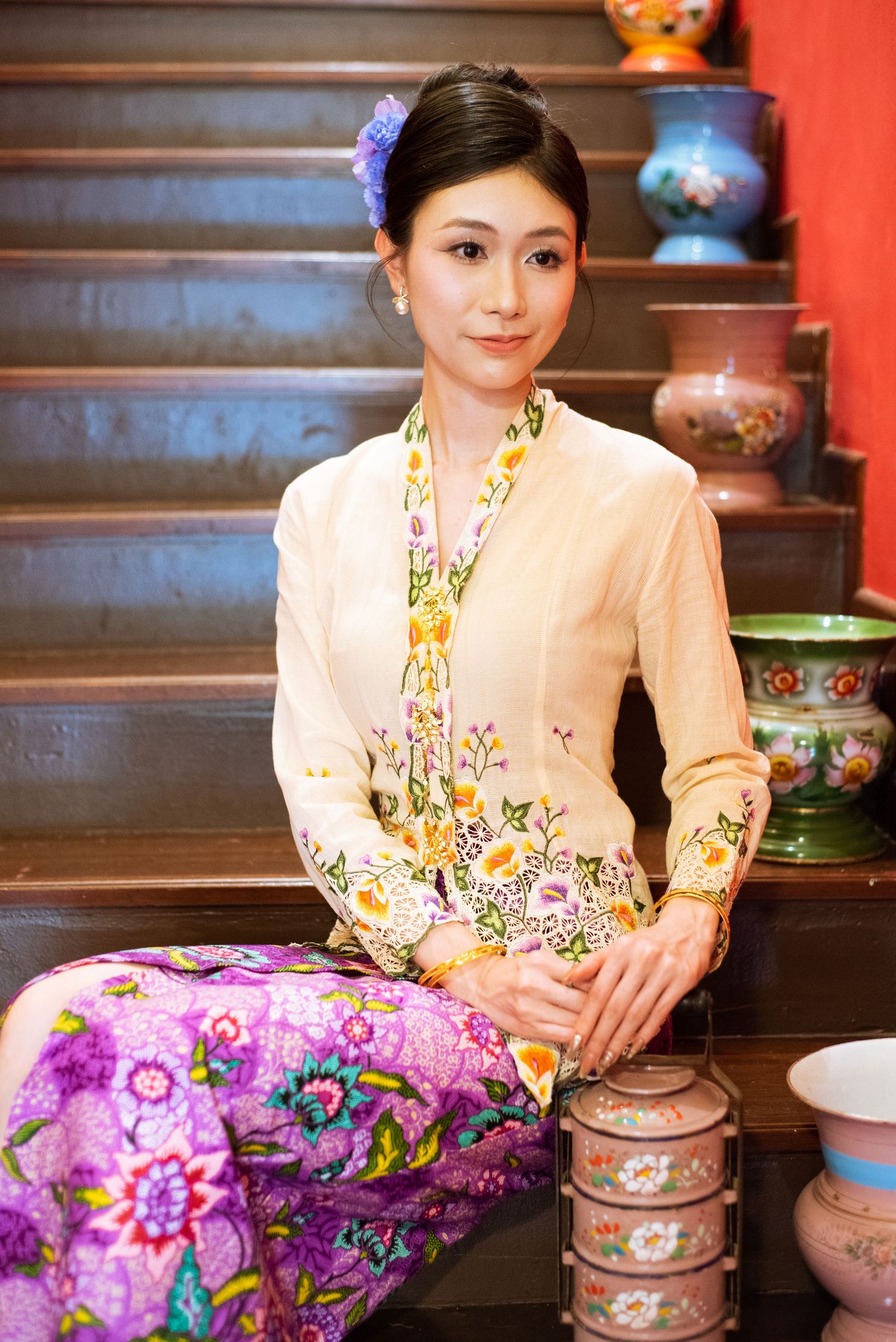 Traditional Peranakan culture on display with beautiful embroidered kebaya and sarong outfit next to antique pottery collection.