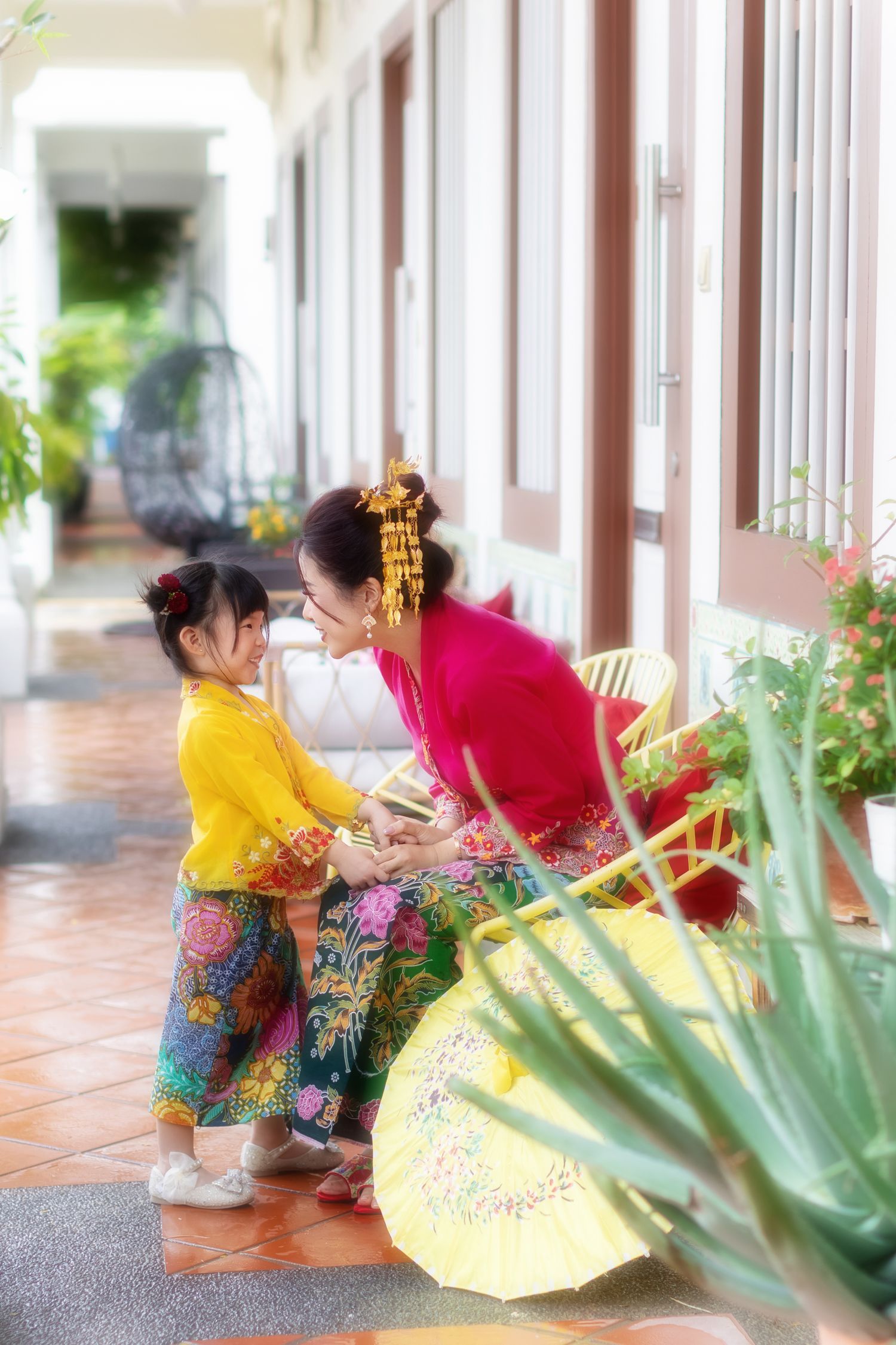 Picture of a Nyonya mother and child in Kebaya and batik sarong, sitting on porch chair at a Peranakan house in Joo Chiat.