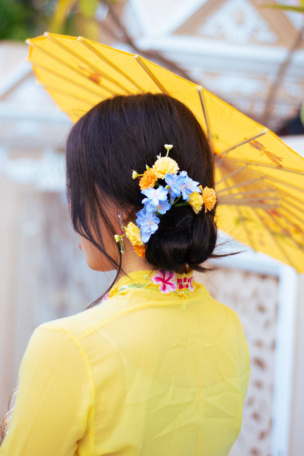 View from behind of traditional Vietnamese outfit in yellow with floral hair decoration and matching parasol.