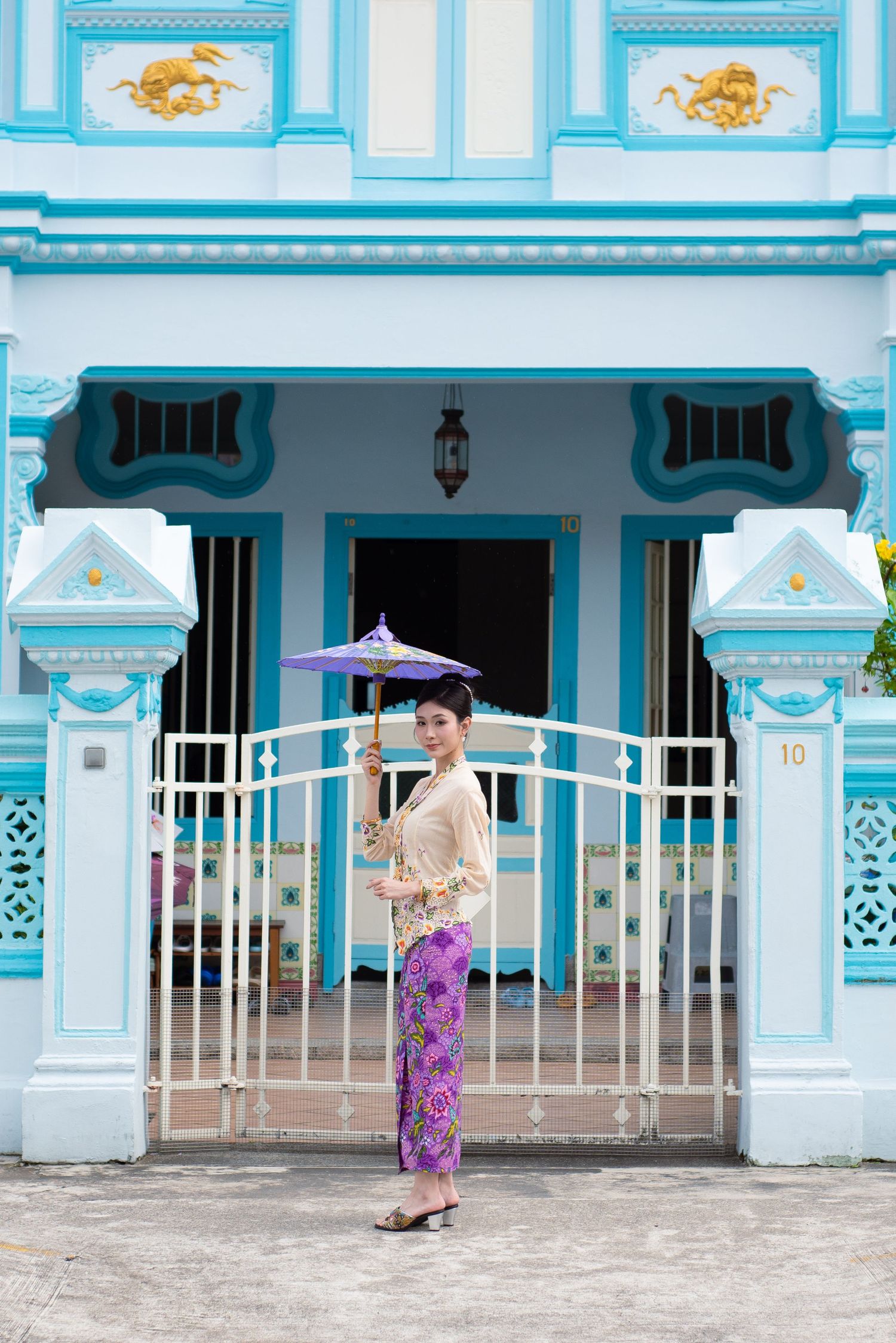 A turquoise heritage building with ornate details frames a scene with a parasol against its decorative entrance.