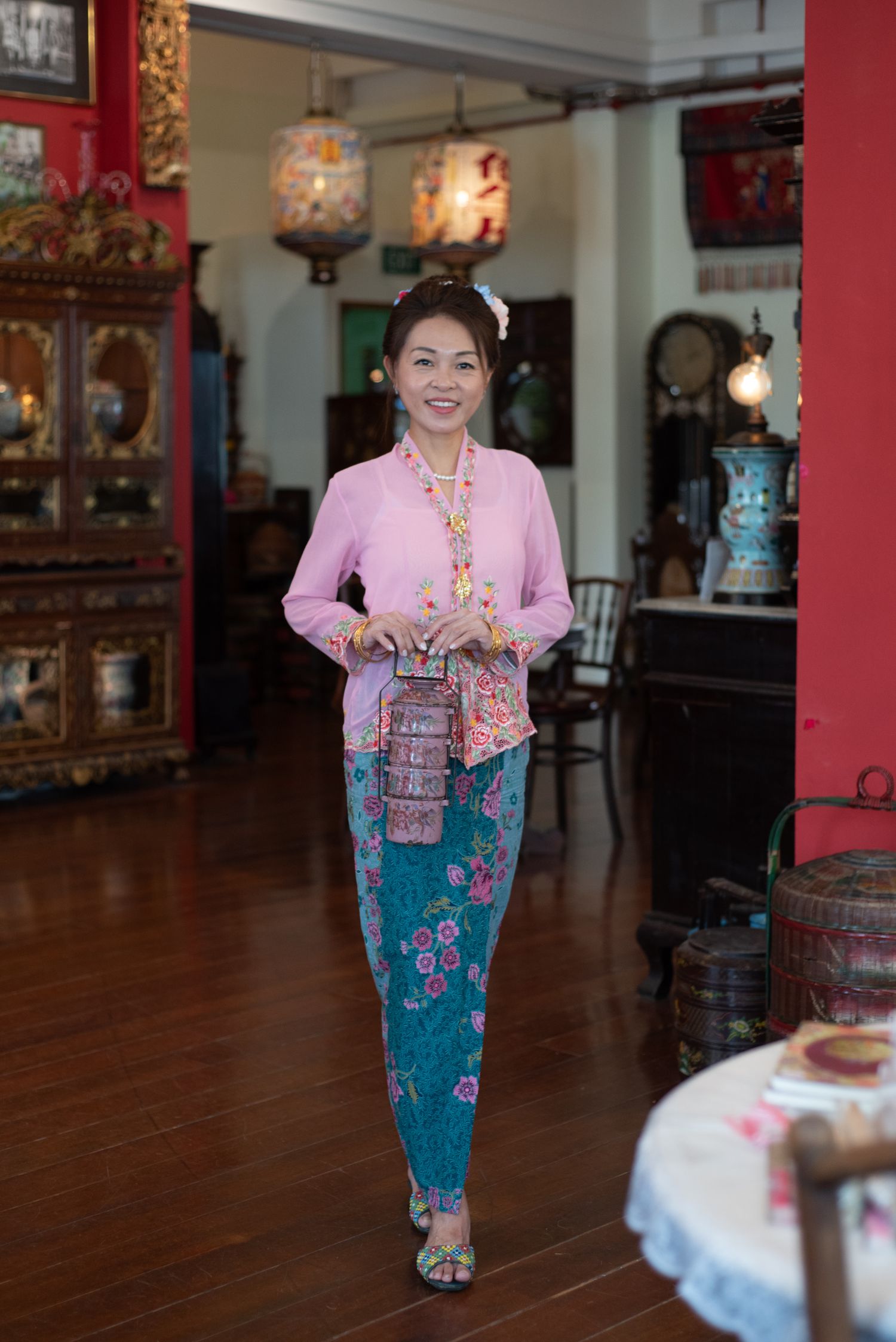 A series of four photos showing someone in traditional Peranakan attire with a pink kebaya top and blue sarong in an ornate interior.