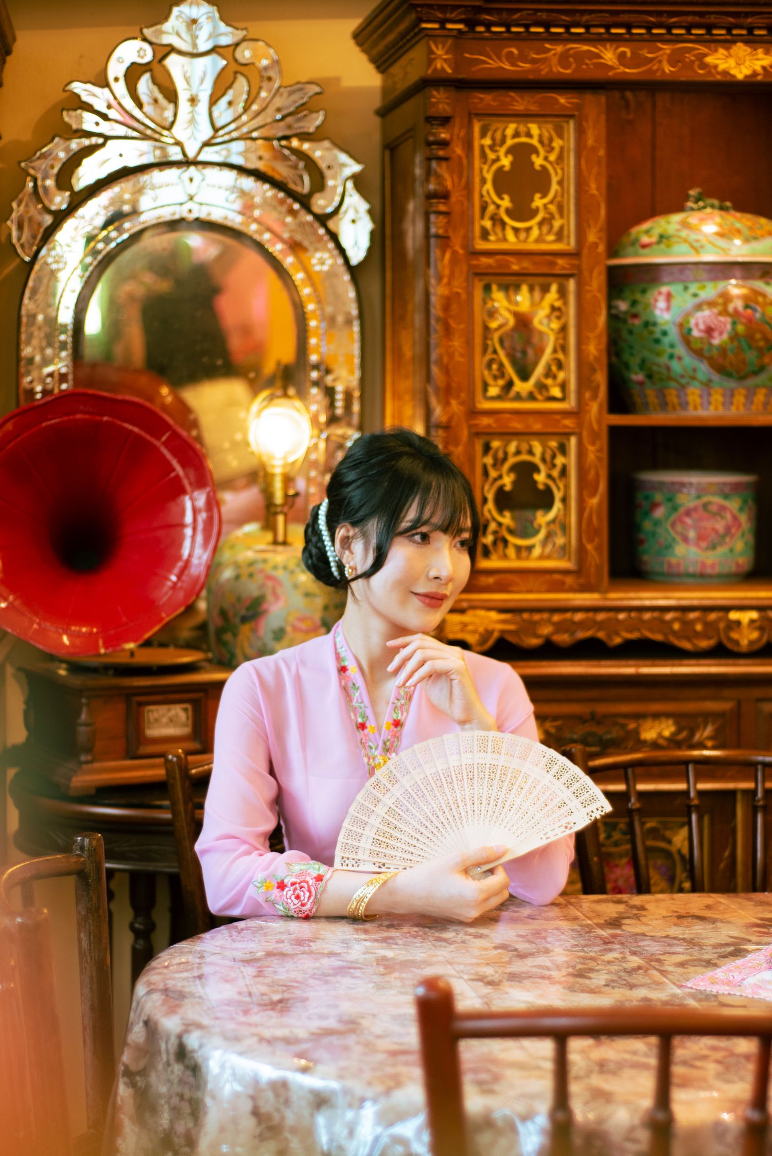 Vintage pink cafe table setting with ornate carved wood decor and lacework tablecloth in warm lighting.