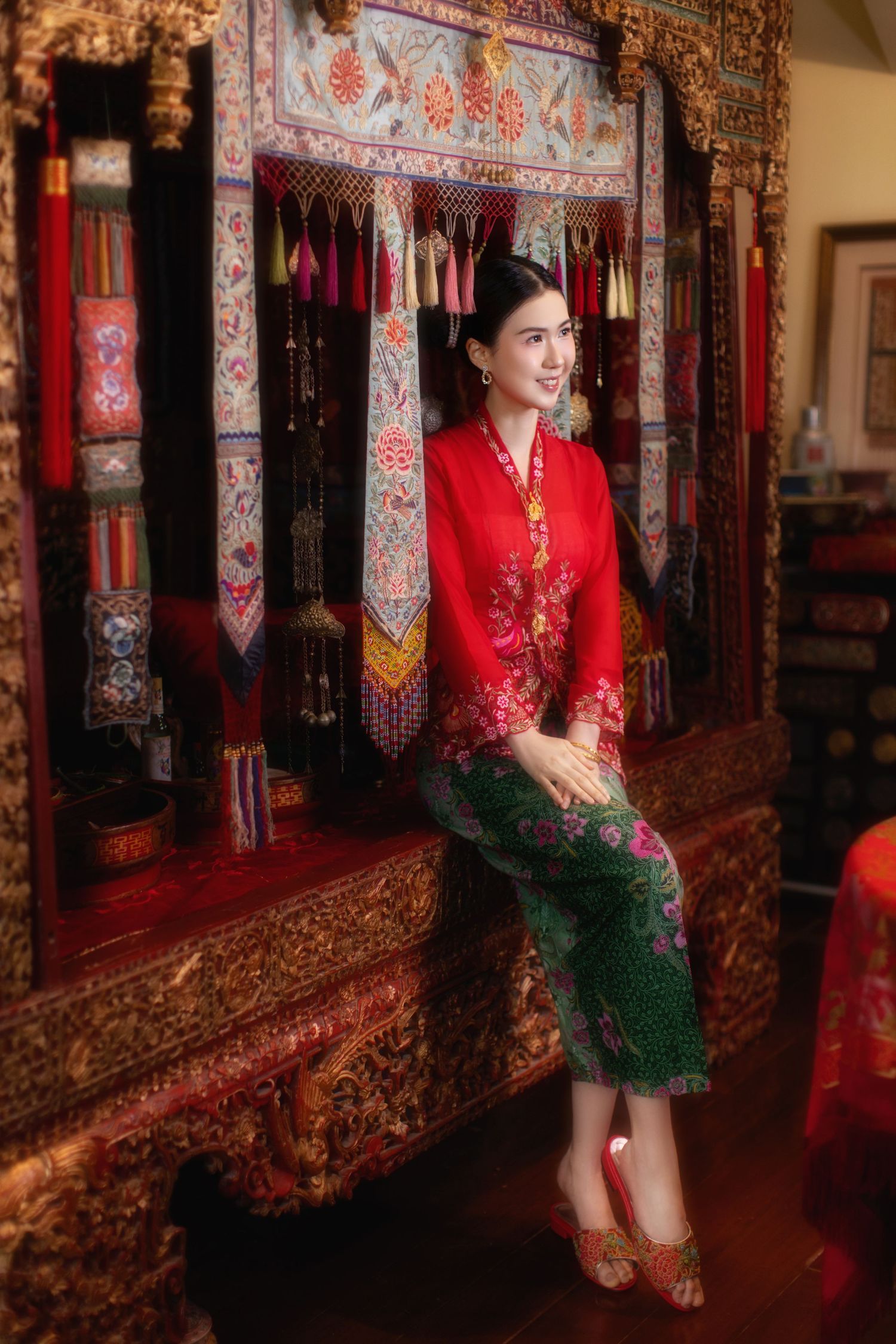 Photo of a Nyonya in a red kebaya, sitting on an antique Peranakan wedding bed, inside a private museum, Peranakan Mansion, at Joo Chiat.