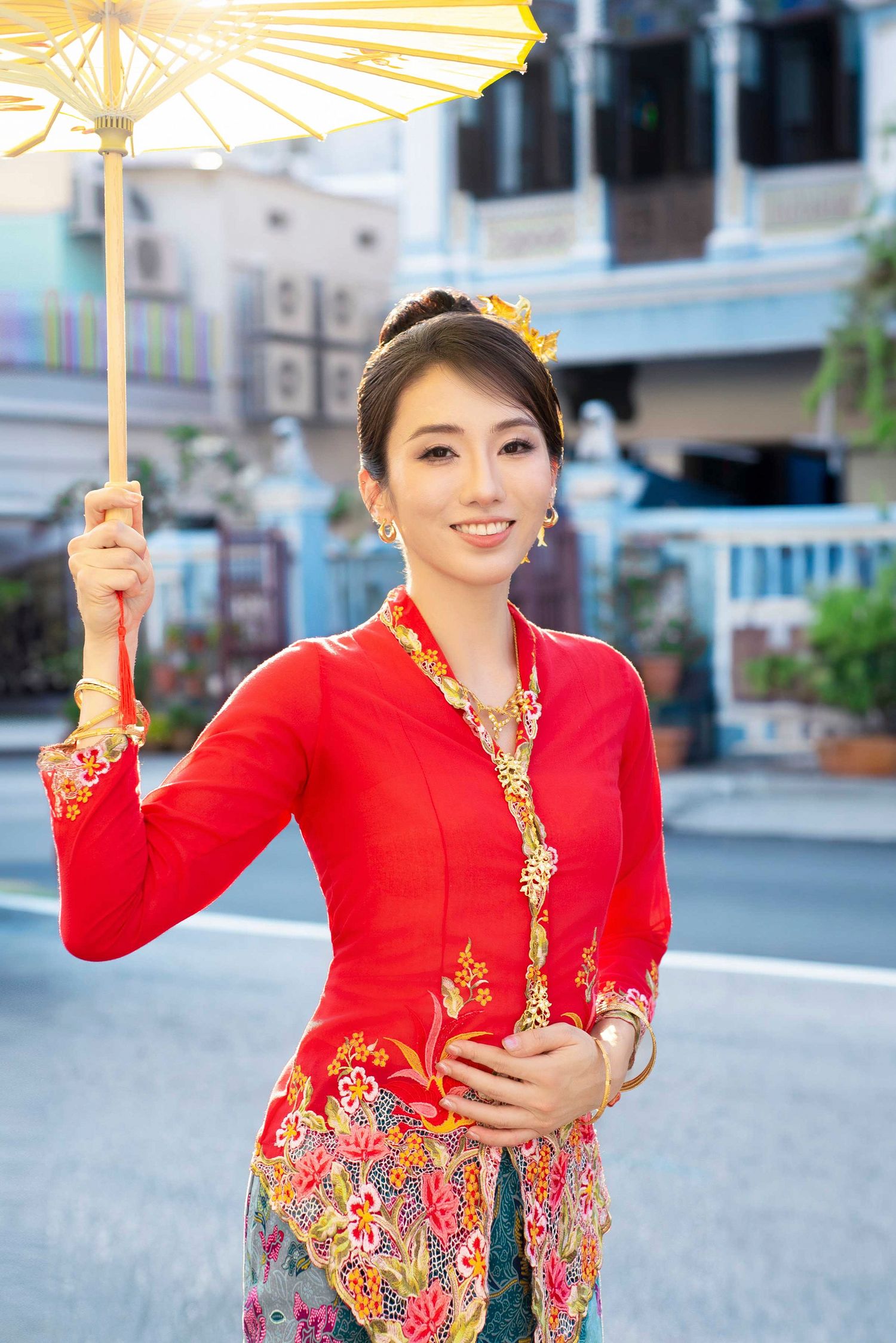 A traditional Thai umbrella holder wearing a red and gold traditional dress with ornate embroidery patterns on a city street.