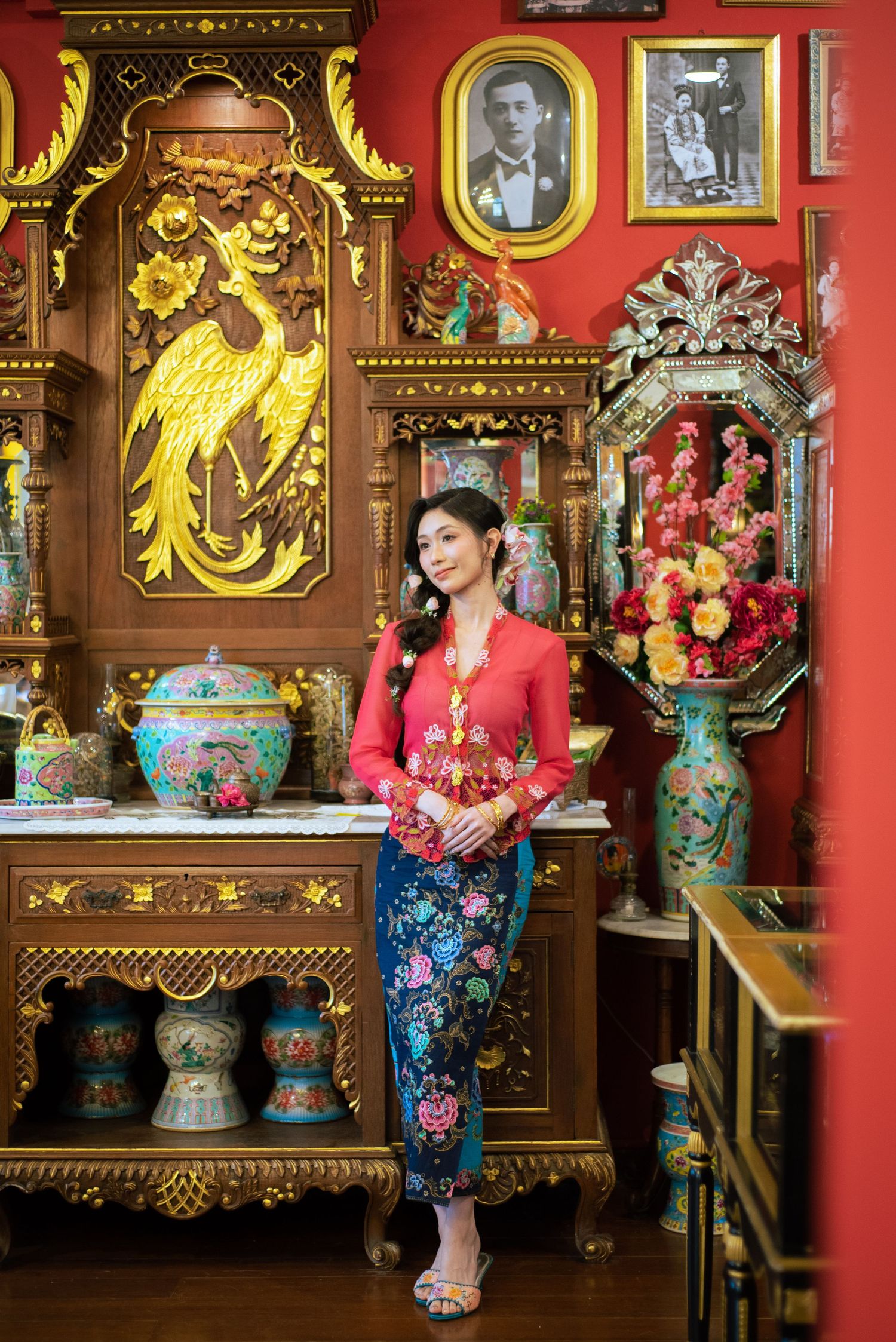 Ornate Asian interior with red walls featuring golden decorative elements, traditional vases, and cultural decor in warm lighting.