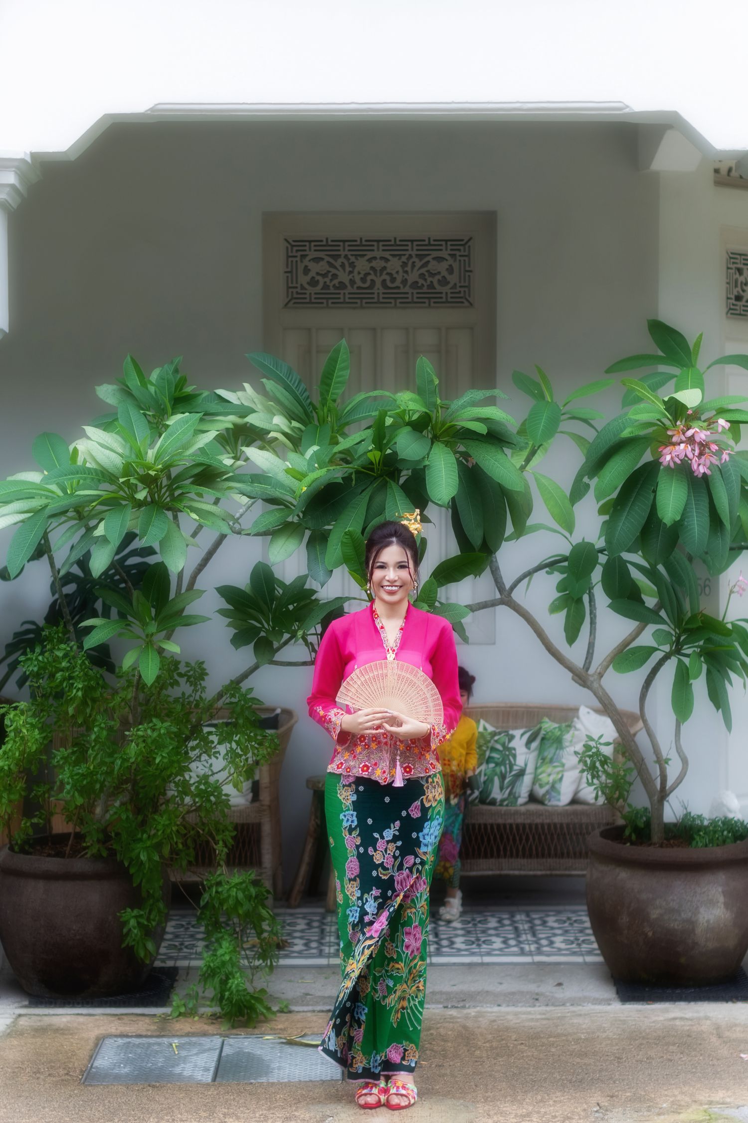 Photo of a Nyonya / Nonya lady in pink kebaya and batik sarong, posing in a courtyard setting at a Peranakan house in Joo Chiat.