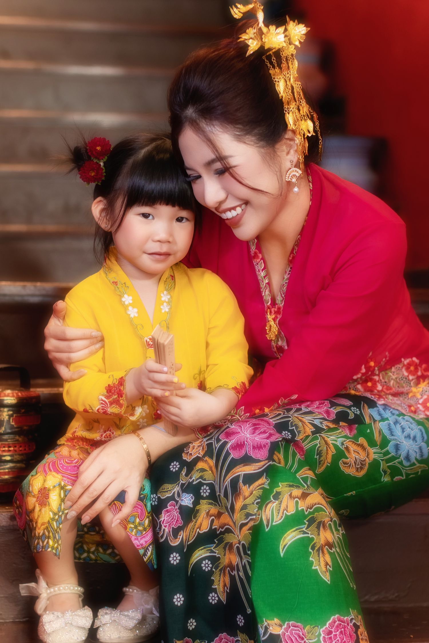 Photoshoot of a Mother and child in traditional Nyonya Kebaya sitting on red-walled stairs in private museum Peranakan Mansion at Joo Chiat.